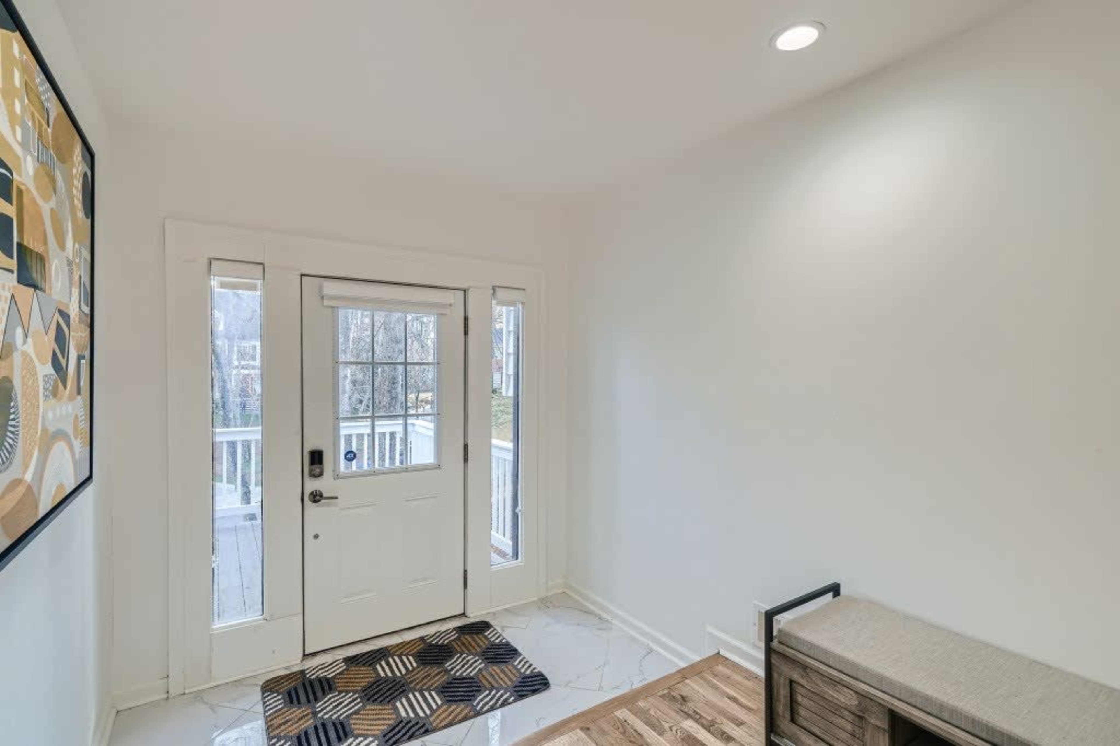 A small entryway with a front door, side windows, a patterned mat, and a bench against the wall.