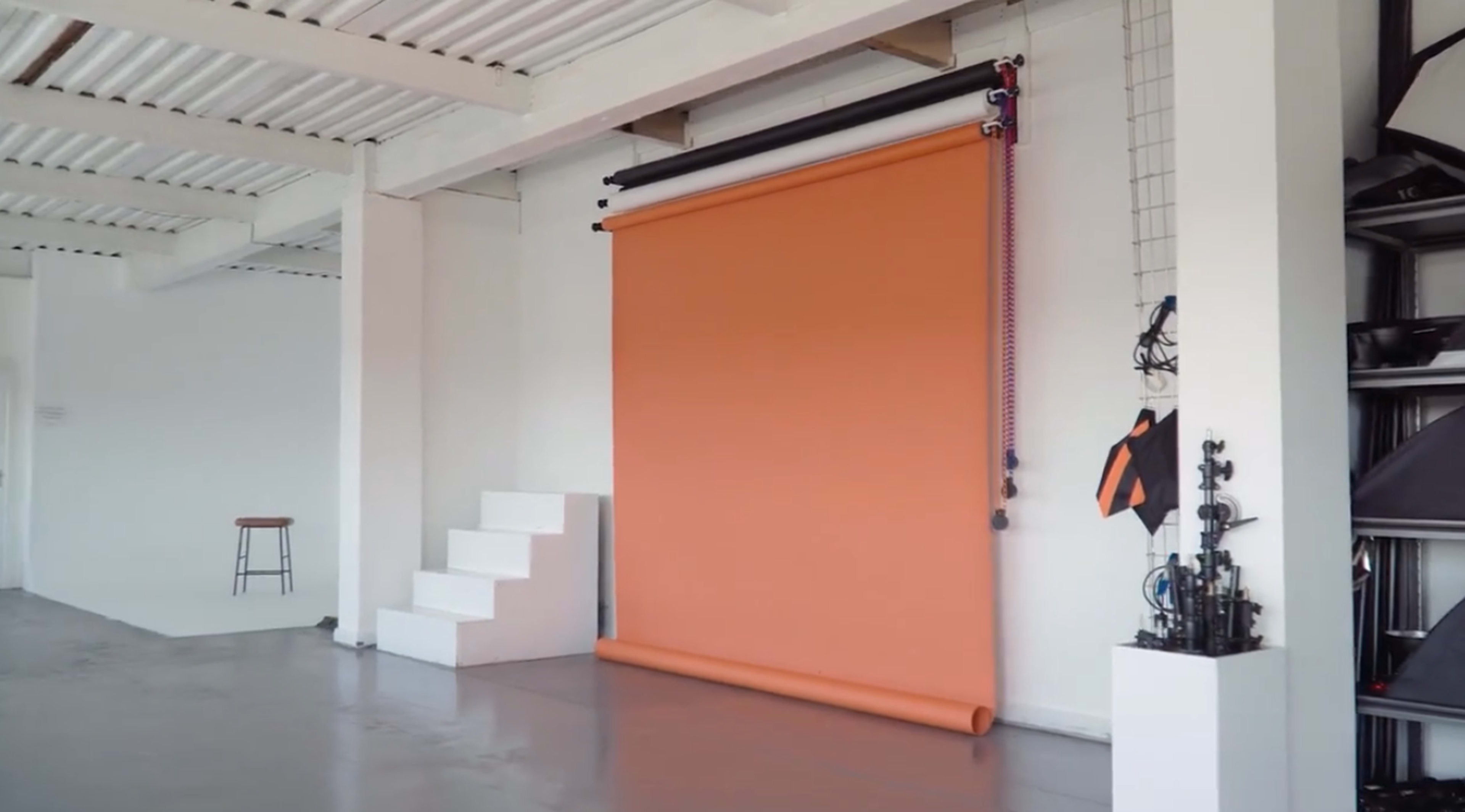 A studio setting featuring an orange backdrop mounted on a wall, a stool, and a set of stairs leading up to it.
