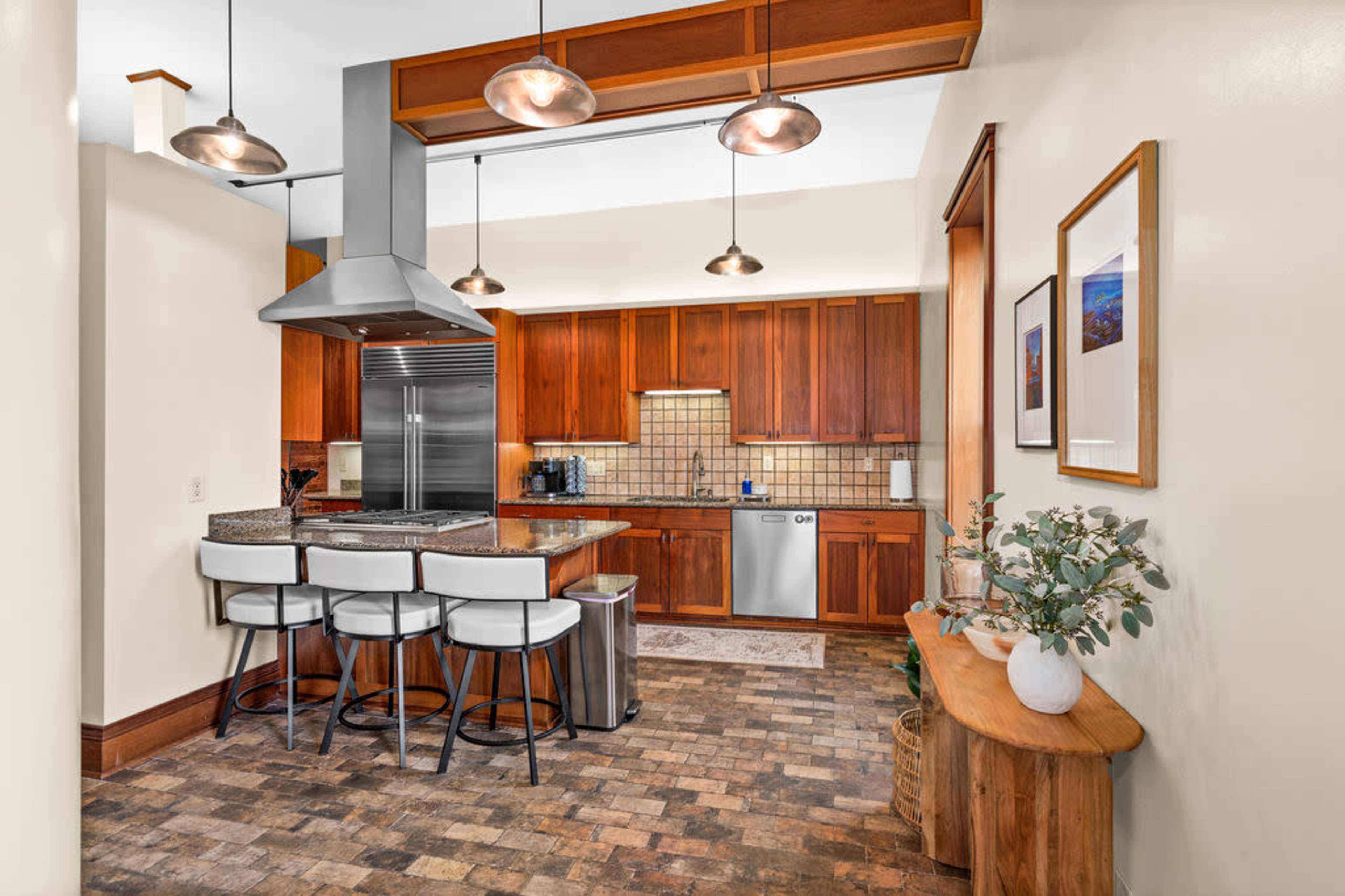 A modern kitchen featuring wooden cabinetry, a central island with bar stools, and stainless steel appliances.
