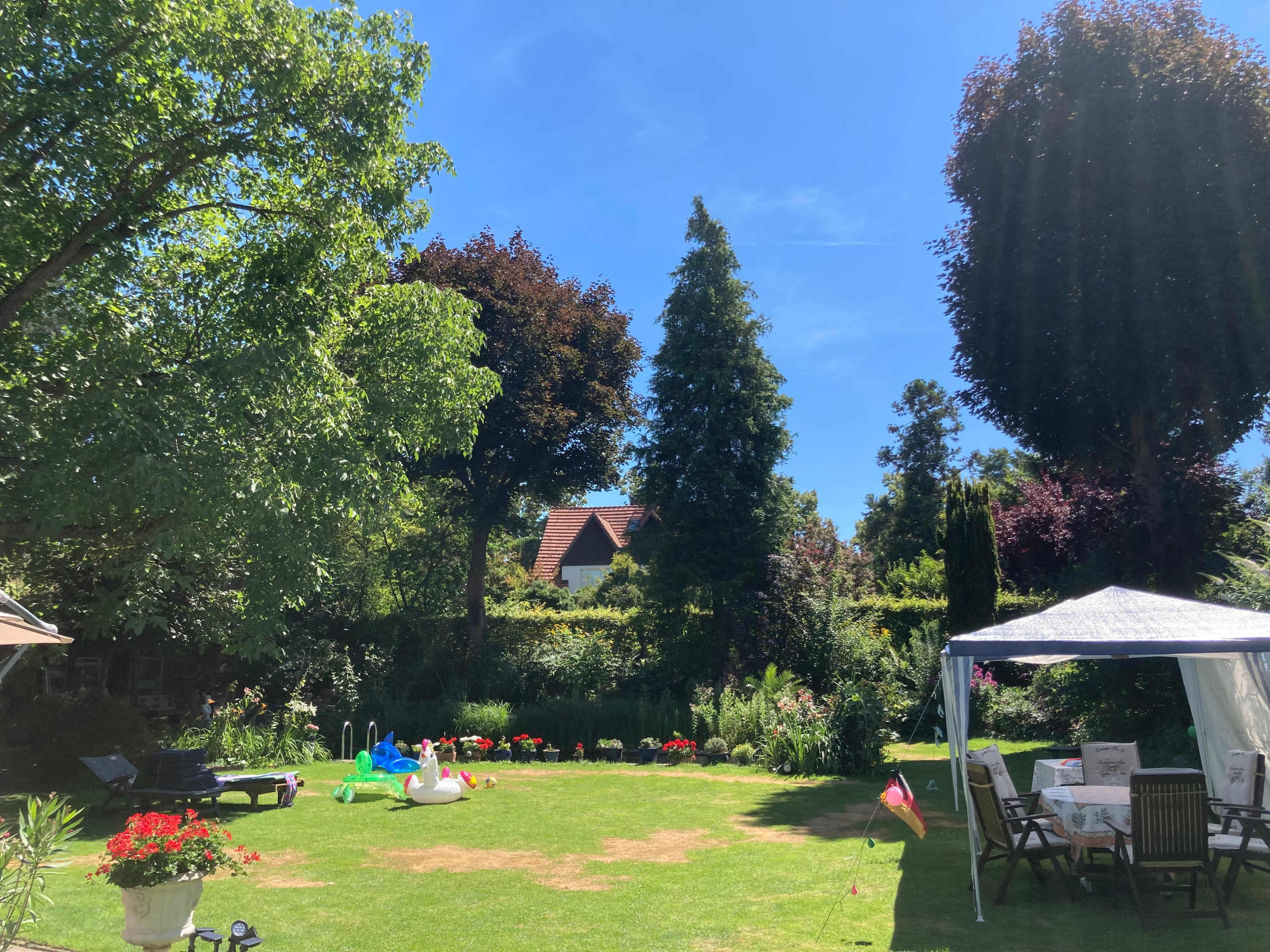 A lush garden features green grass, colorful flowers, and a gazebo under a clear blue sky.
