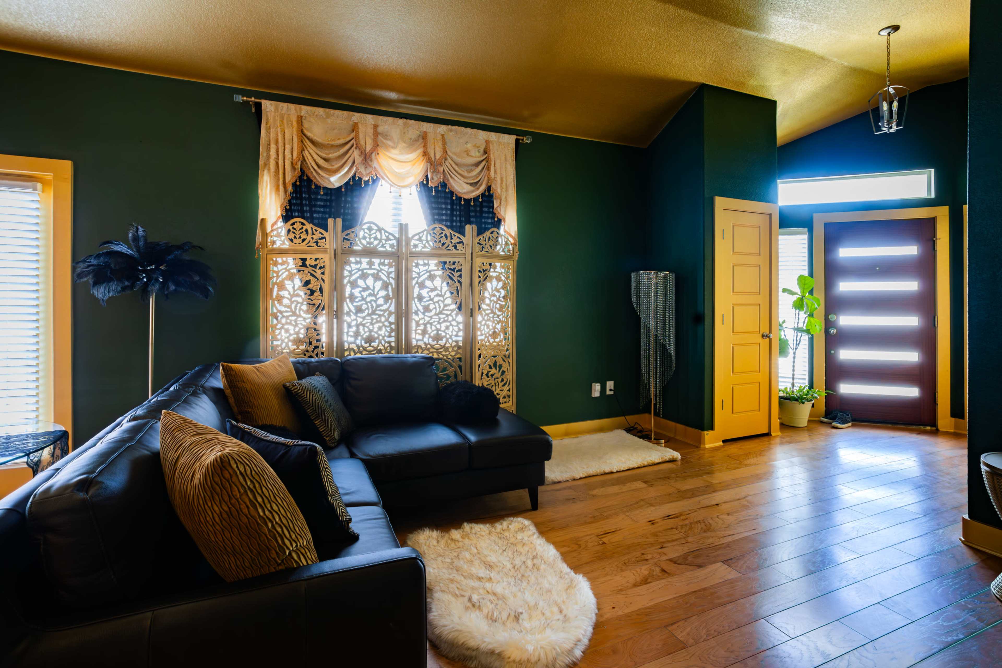 A living room with a black sectional sofa, decorative pillows, a patterned screen, and a front door illuminated by natural light.