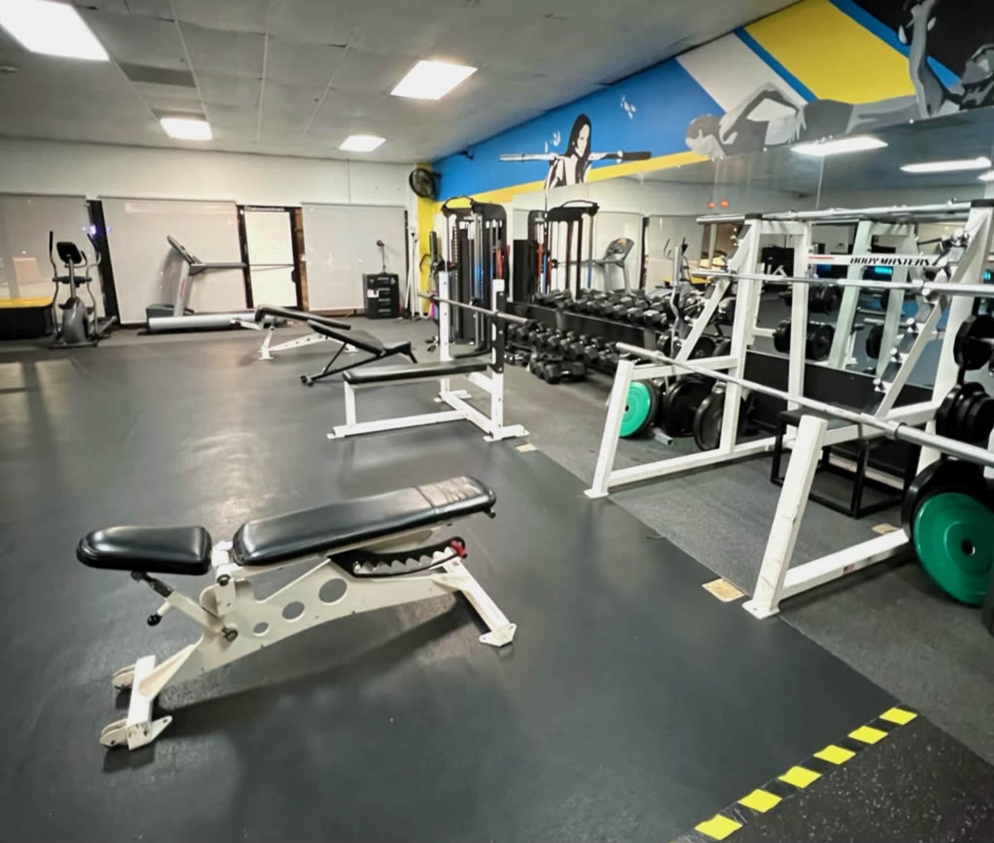 A fitness gym with various weightlifting equipment, benches, and cardio machines in a well-lit space.