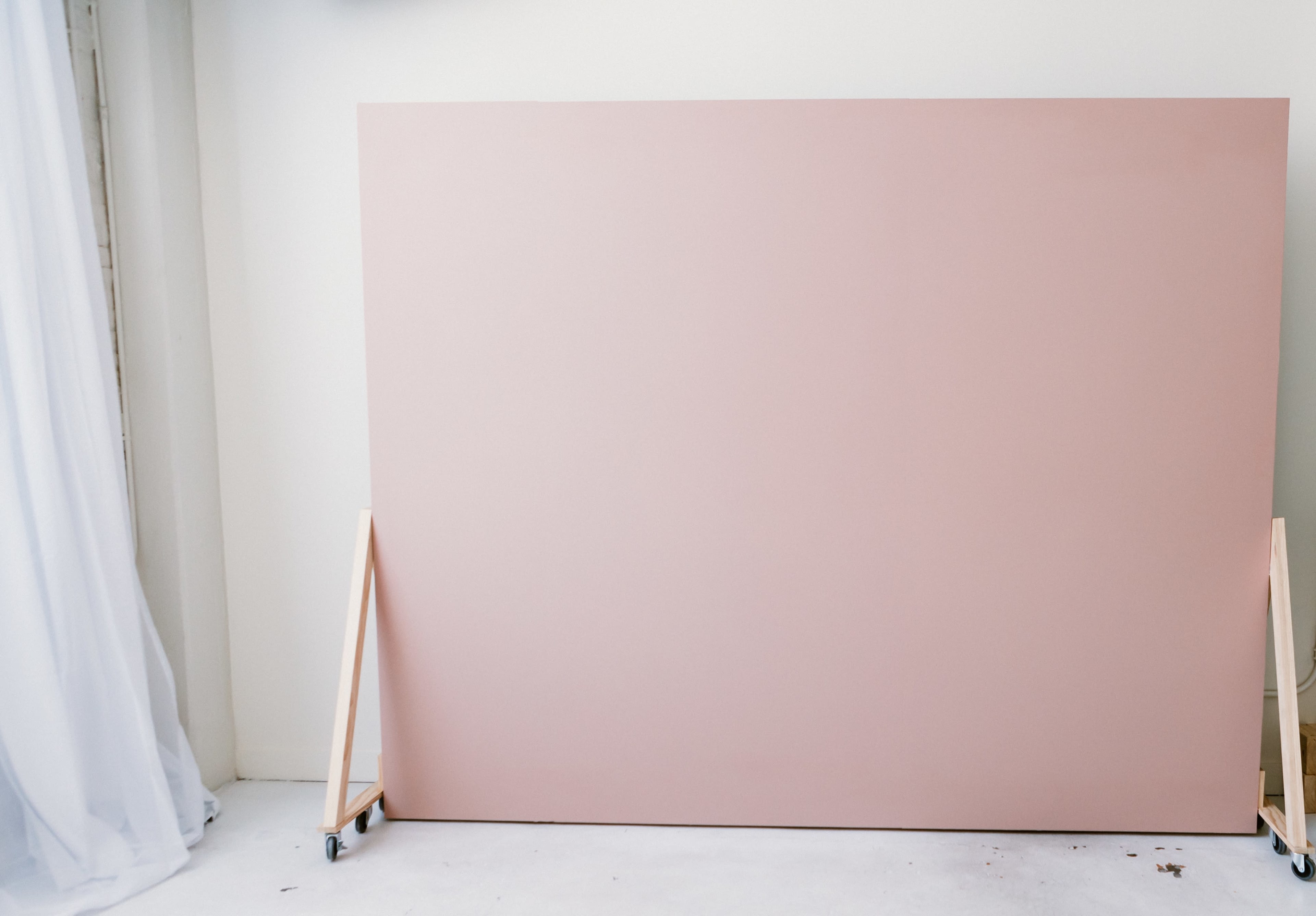 A large, flat, pink panel is positioned on two wooden supports against a light-colored wall.