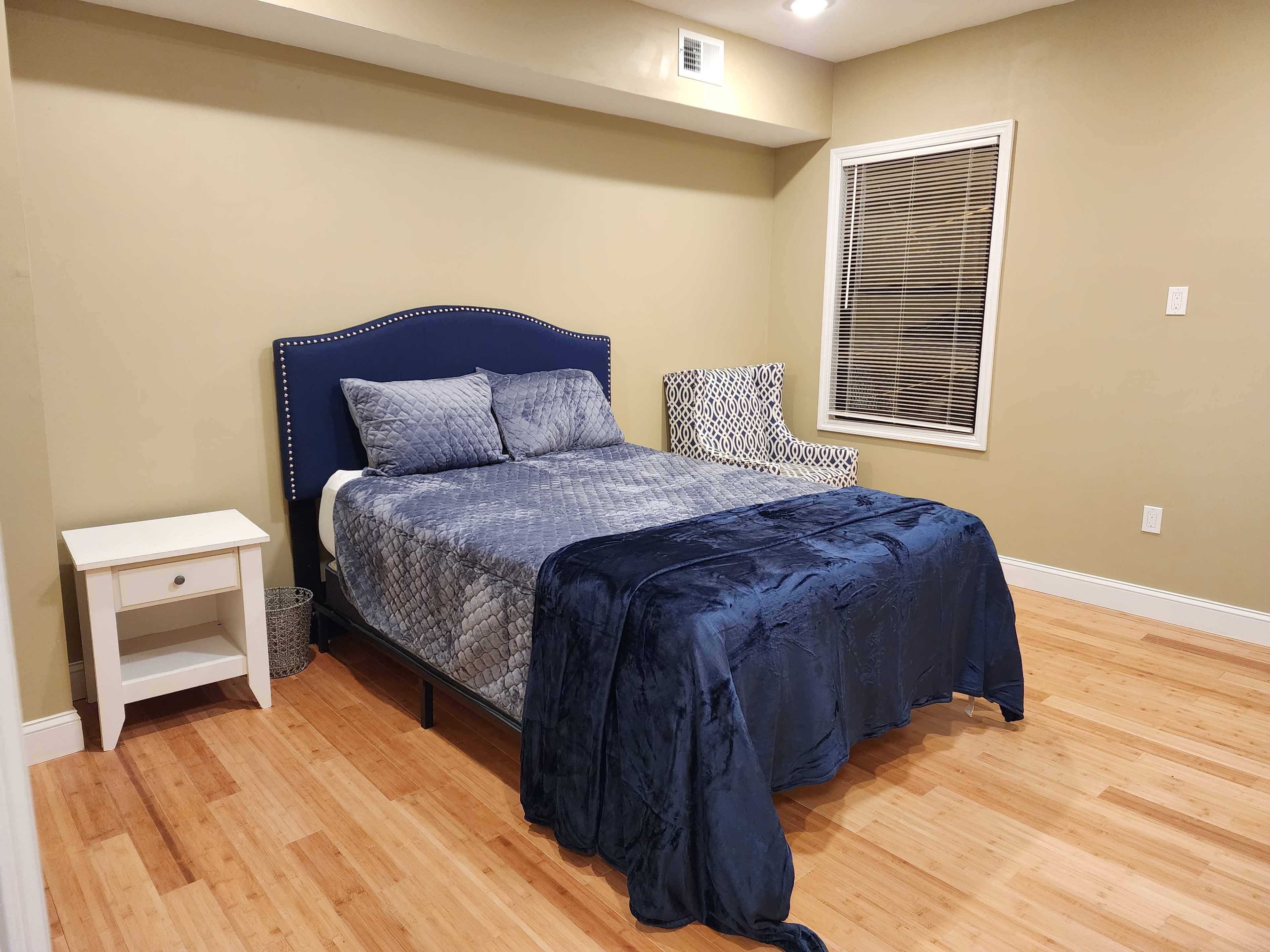 A bedroom with a bed, a side table, and a patterned chair against a green wall.