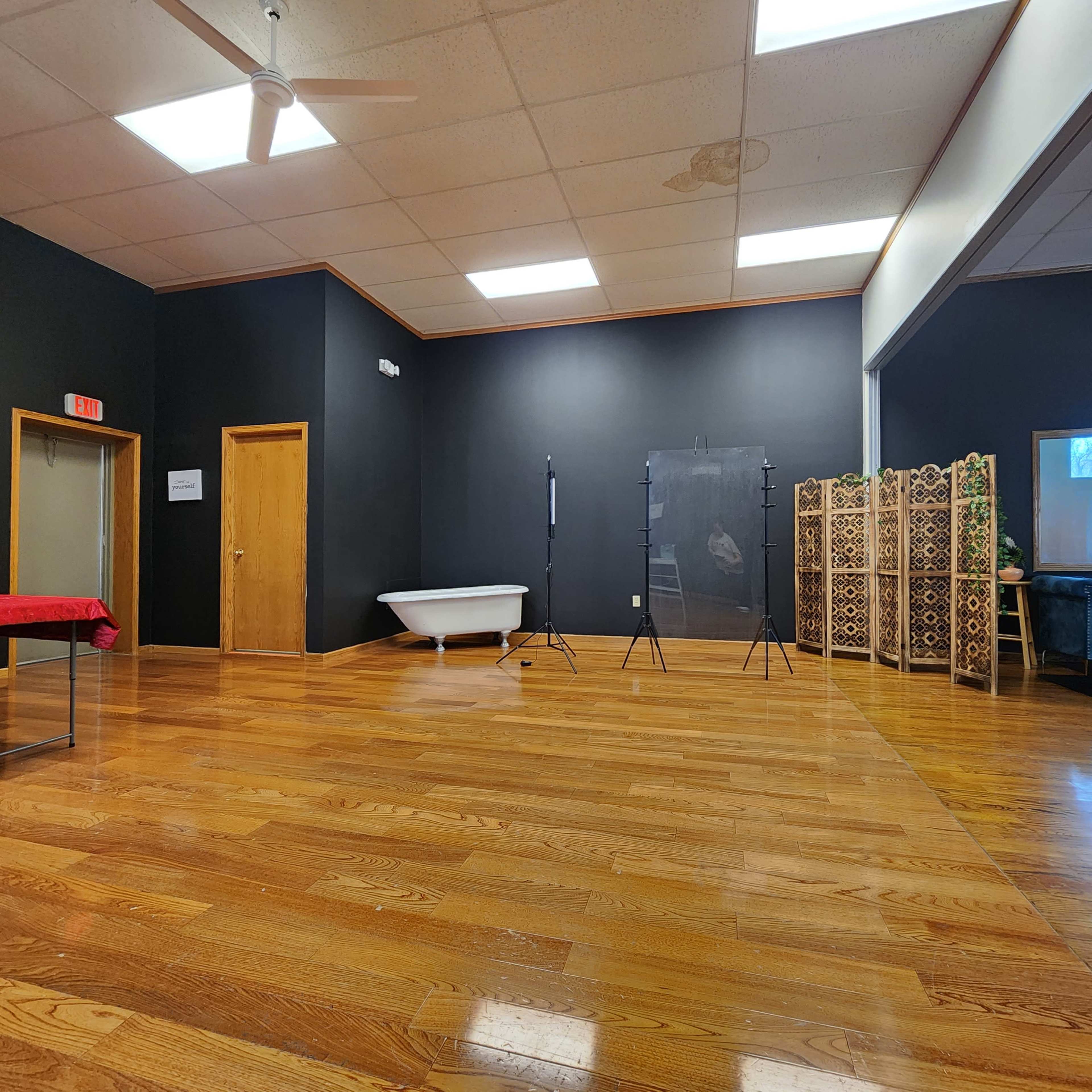 An empty room with dark walls, a wooden floor, a vintage bathtub, and two photo backdrop stands.