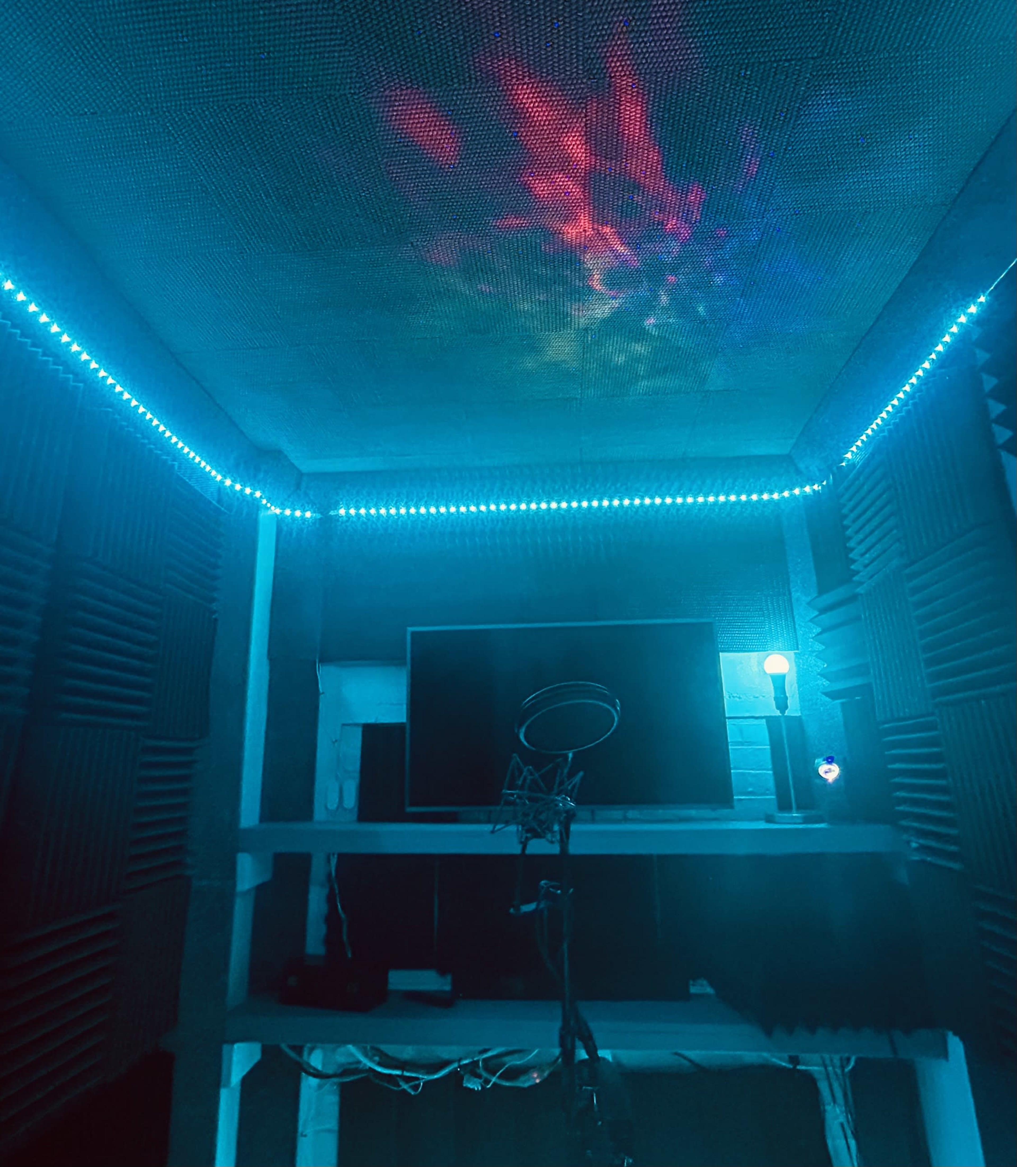 The image shows a sound booth with acoustic panels, a microphone on a stand, and blue LED lighting along the ceiling.