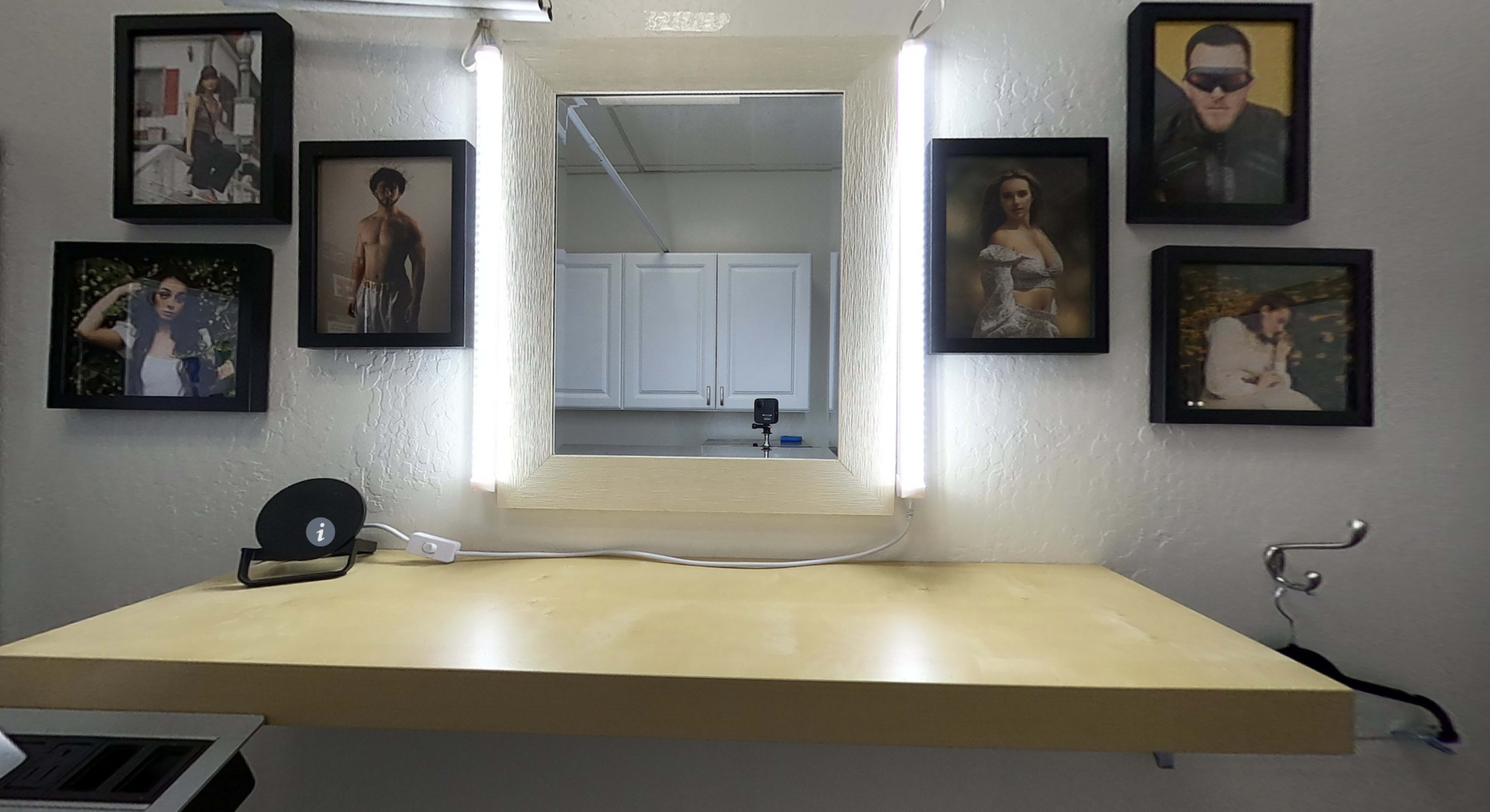 A wall-mounted mirror surrounded by framed photographs, with a wooden table and a record player positioned beneath it.
