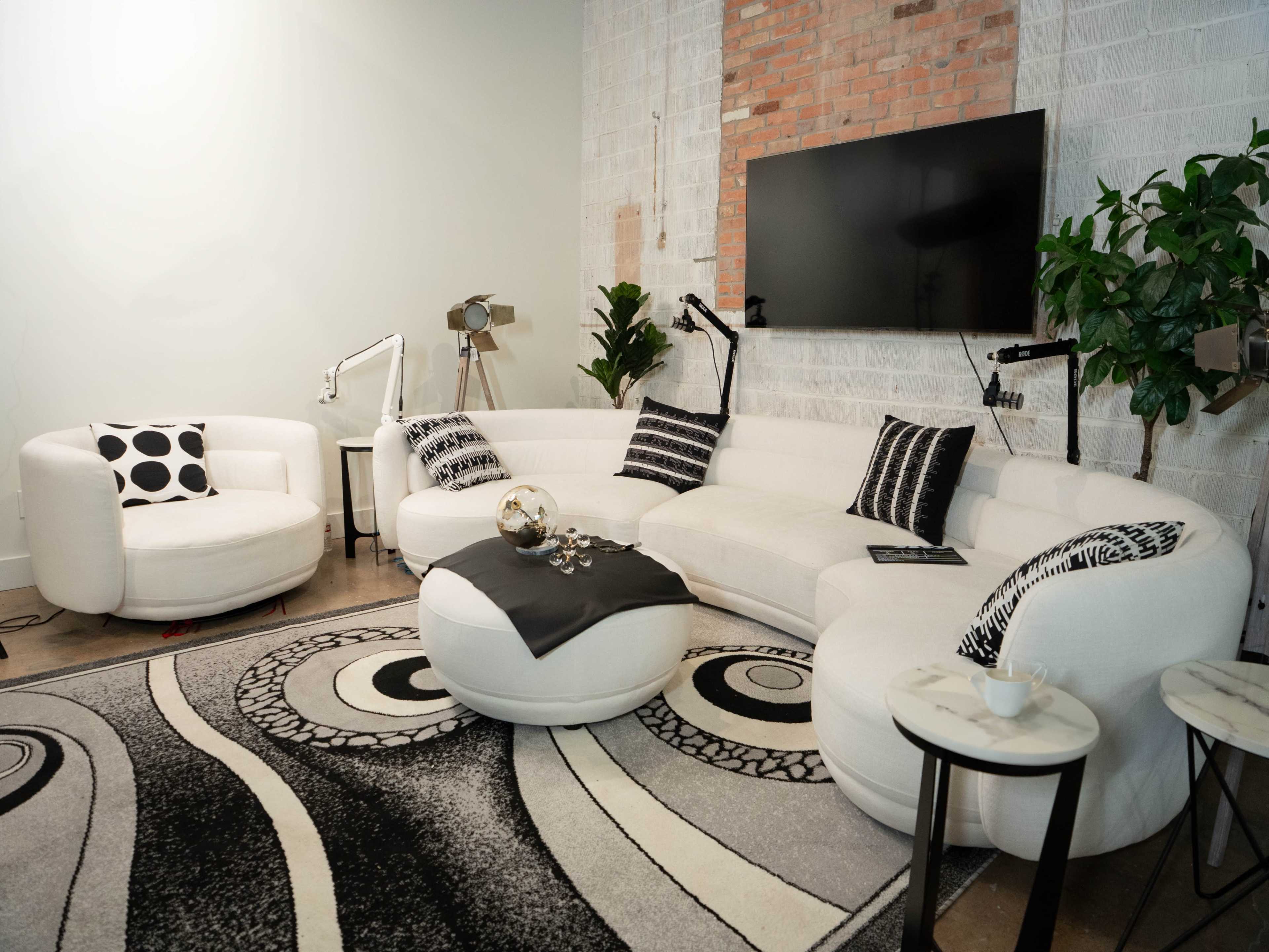 A modern living room features a curved white sofa with black and white patterned pillows, accompanied by a round coffee table and a decorative rug.