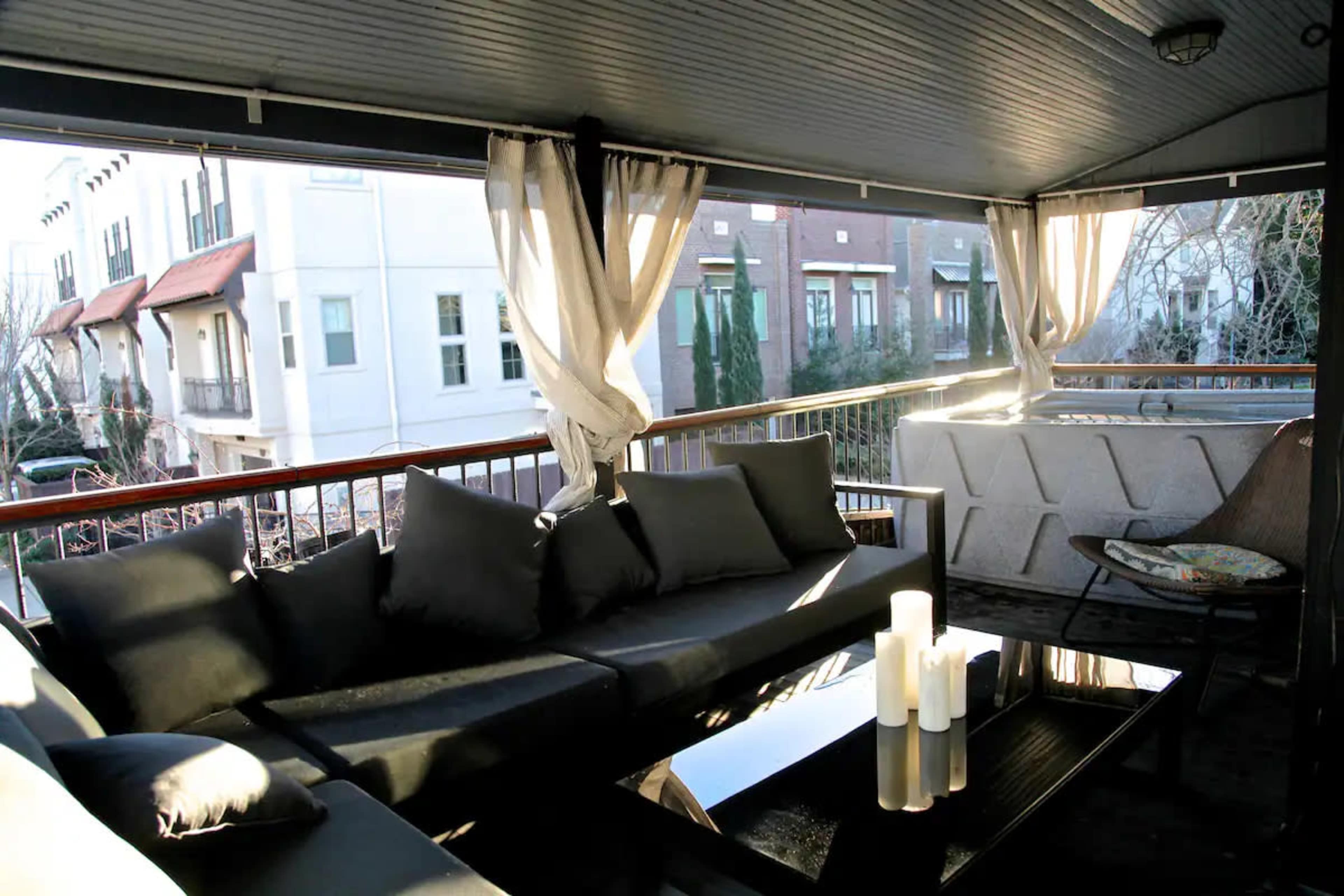 A covered balcony with a sectional sofa, coffee table, and candles, overlooking another building.