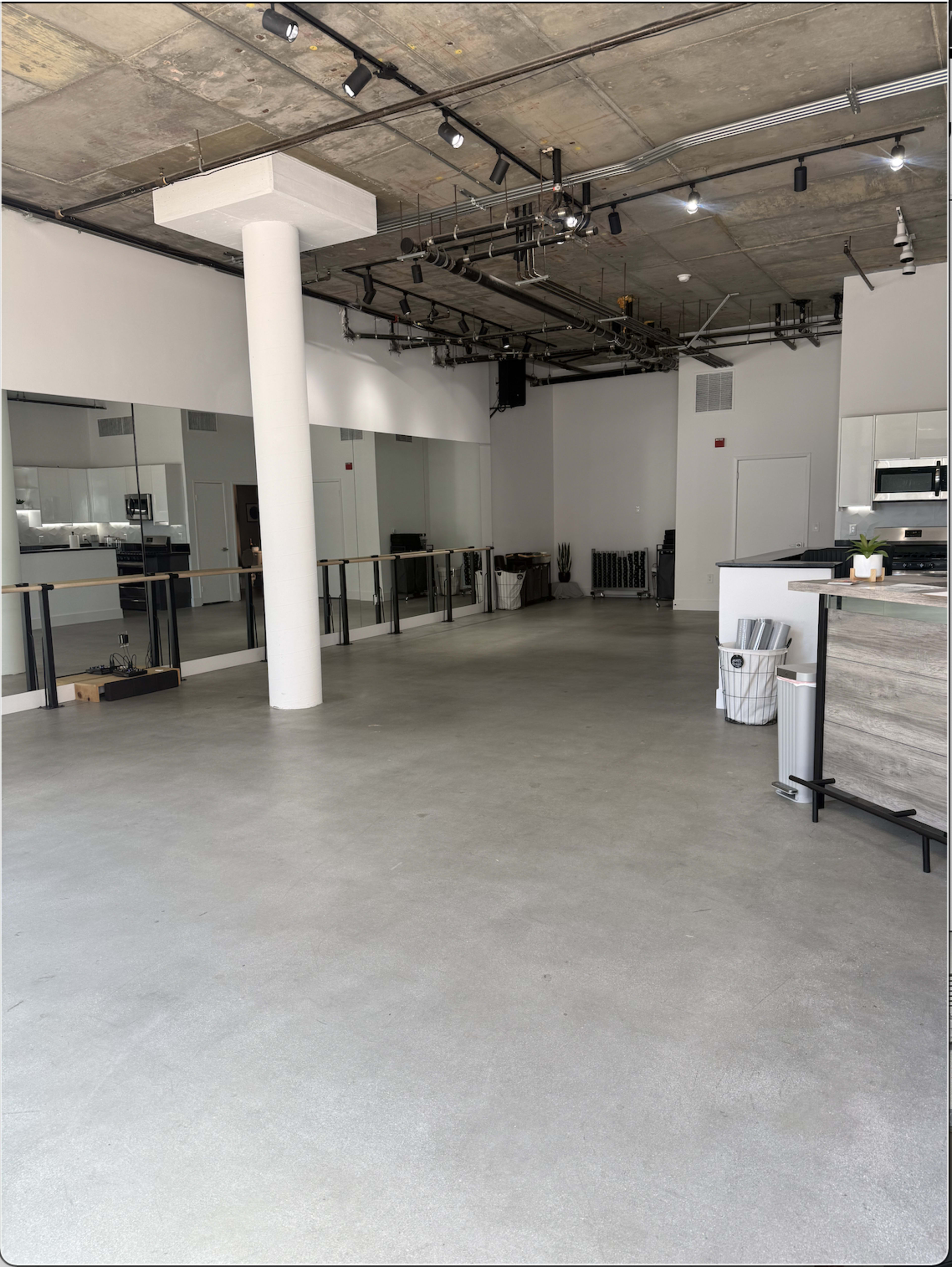 The image shows a spacious, empty interior with polished concrete flooring, large mirrors on one wall, and minimalist kitchen elements in a corner.