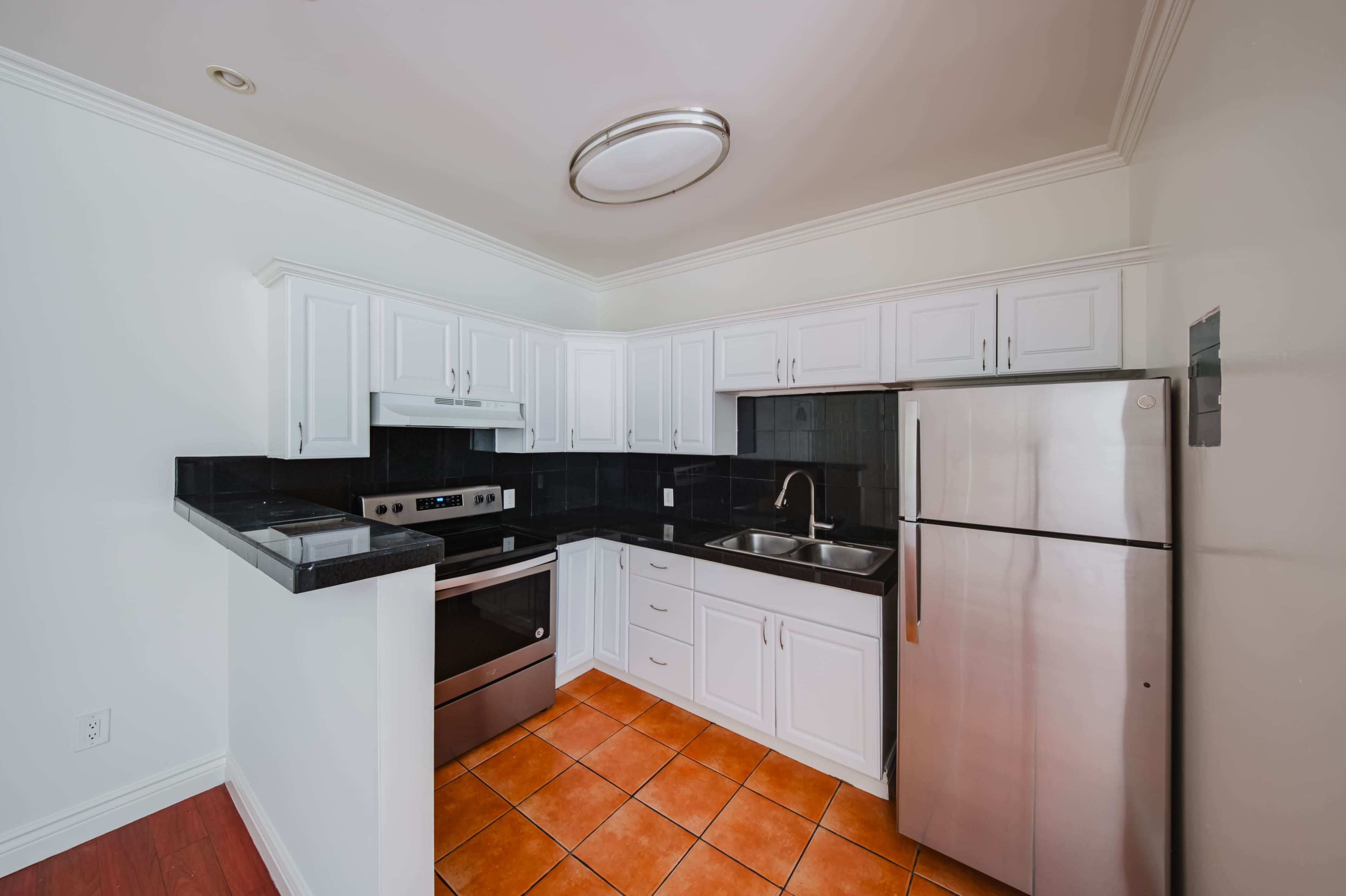 The image shows a modern kitchen with white cabinetry, a stainless steel refrigerator, and a dark countertop.