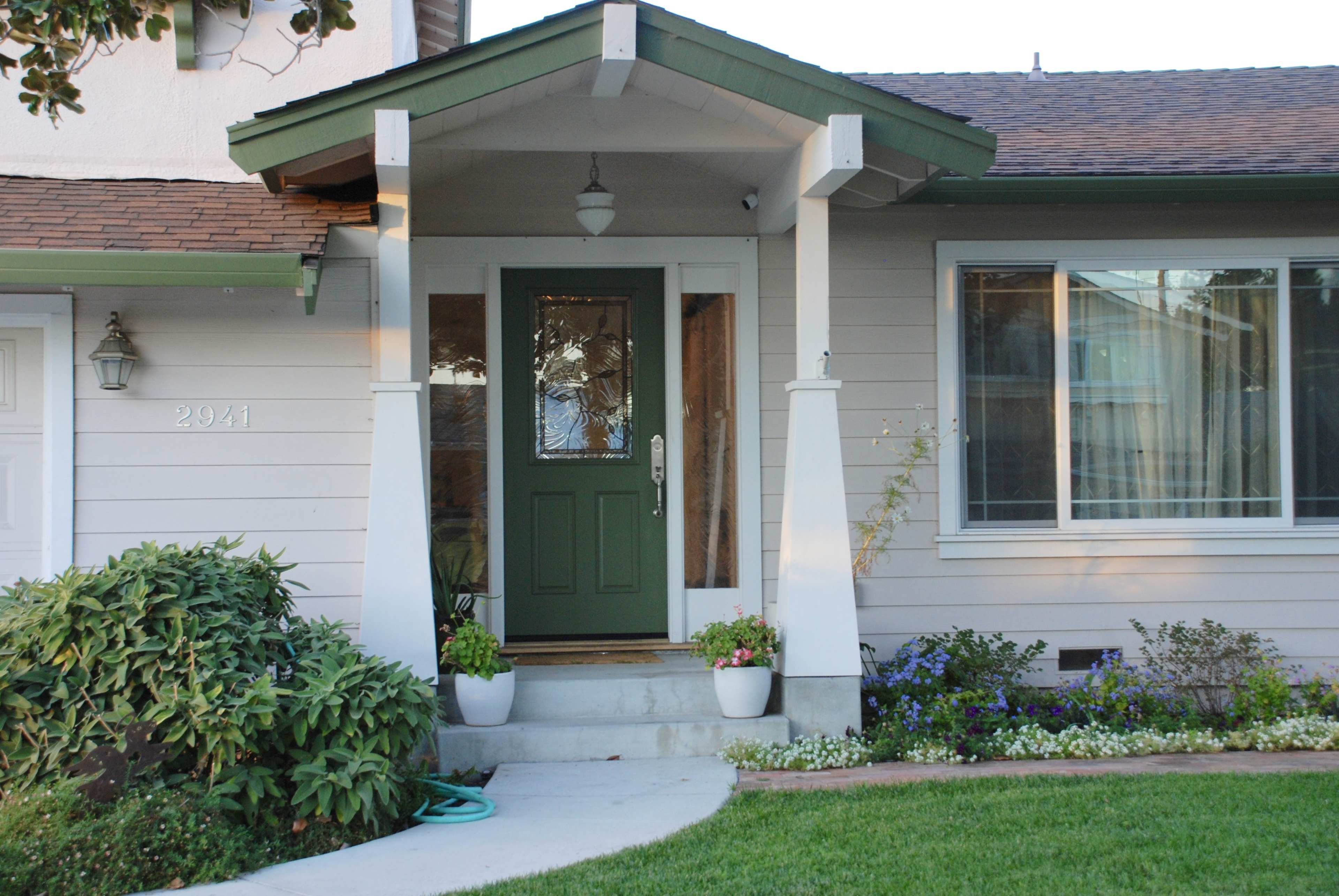 A front porch with a green door and decorative potted plants, leading to a single-story house.