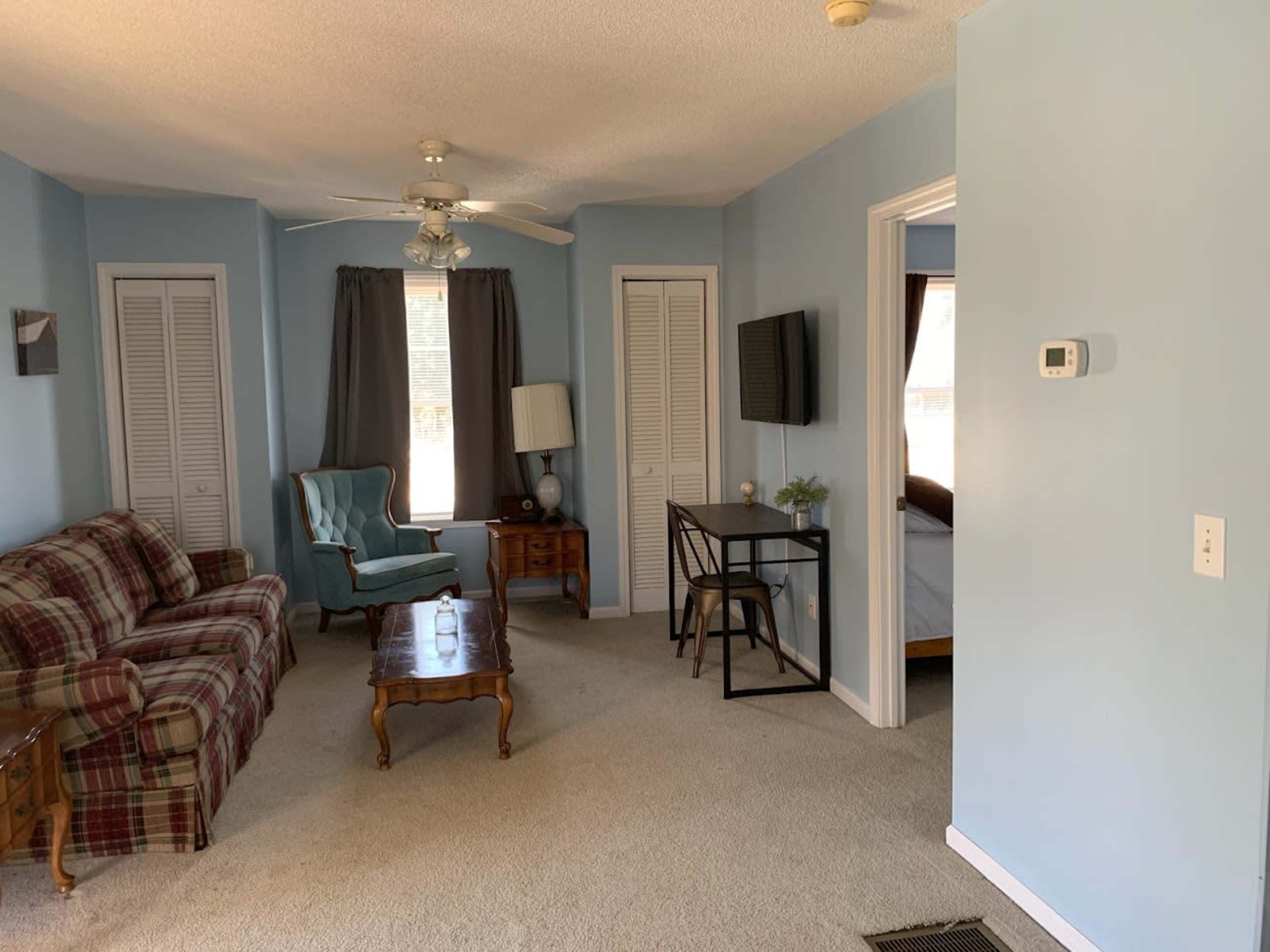 The room features a green armchair, a plaid couch, a coffee table, and a desk against light blue walls.