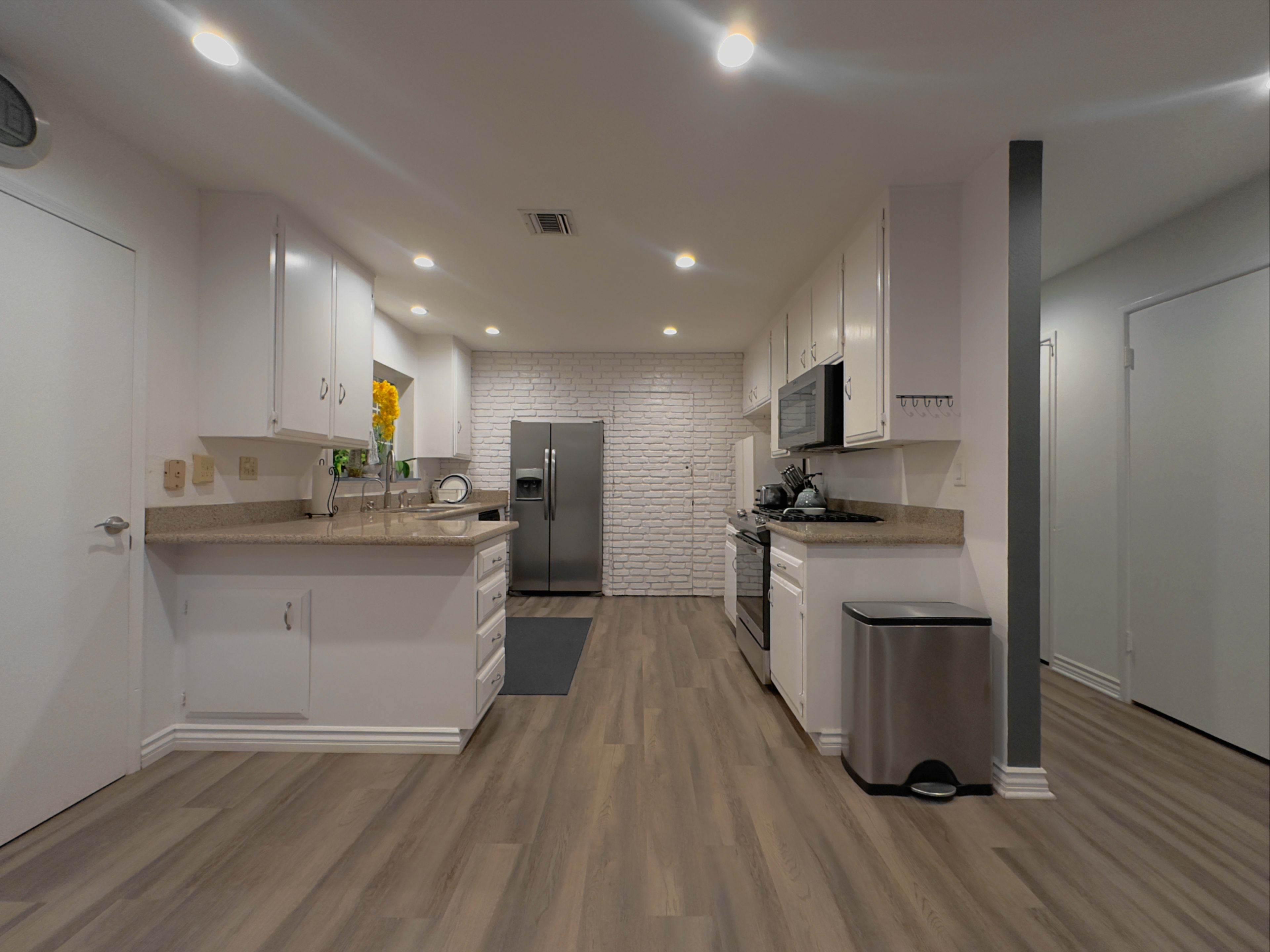A modern kitchen features white cabinetry, stainless steel appliances, and a brick accent wall.