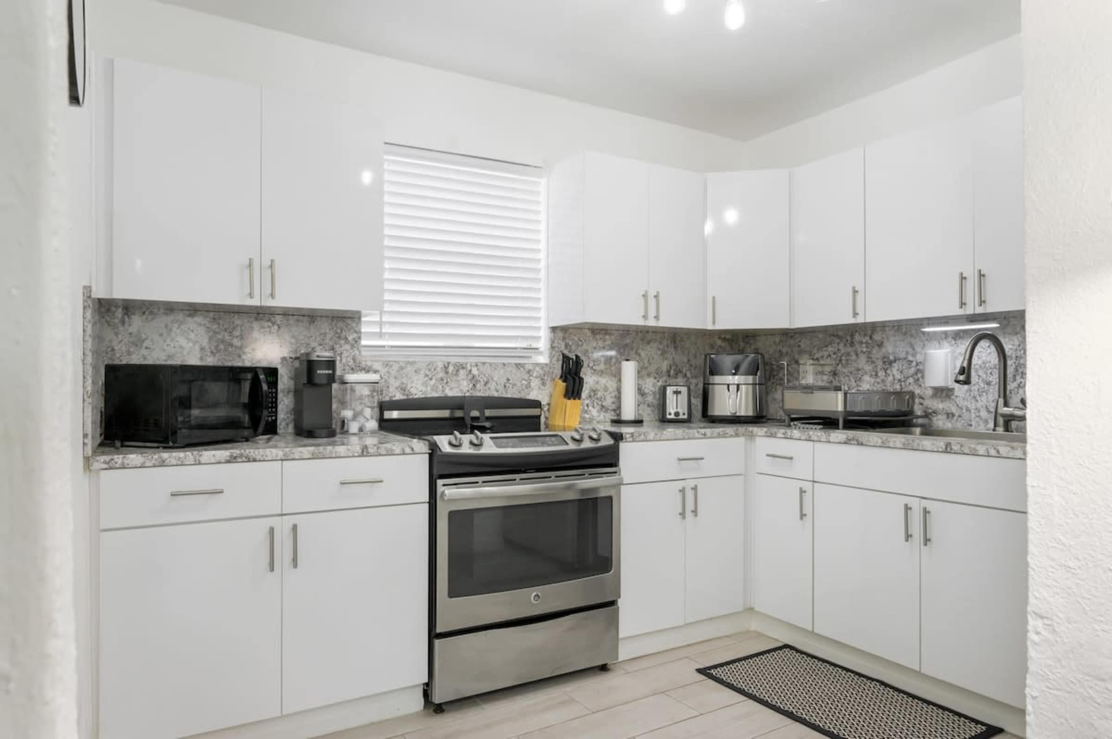 The image shows a modern kitchen with white cabinets, stainless steel appliances, and a marble countertop.