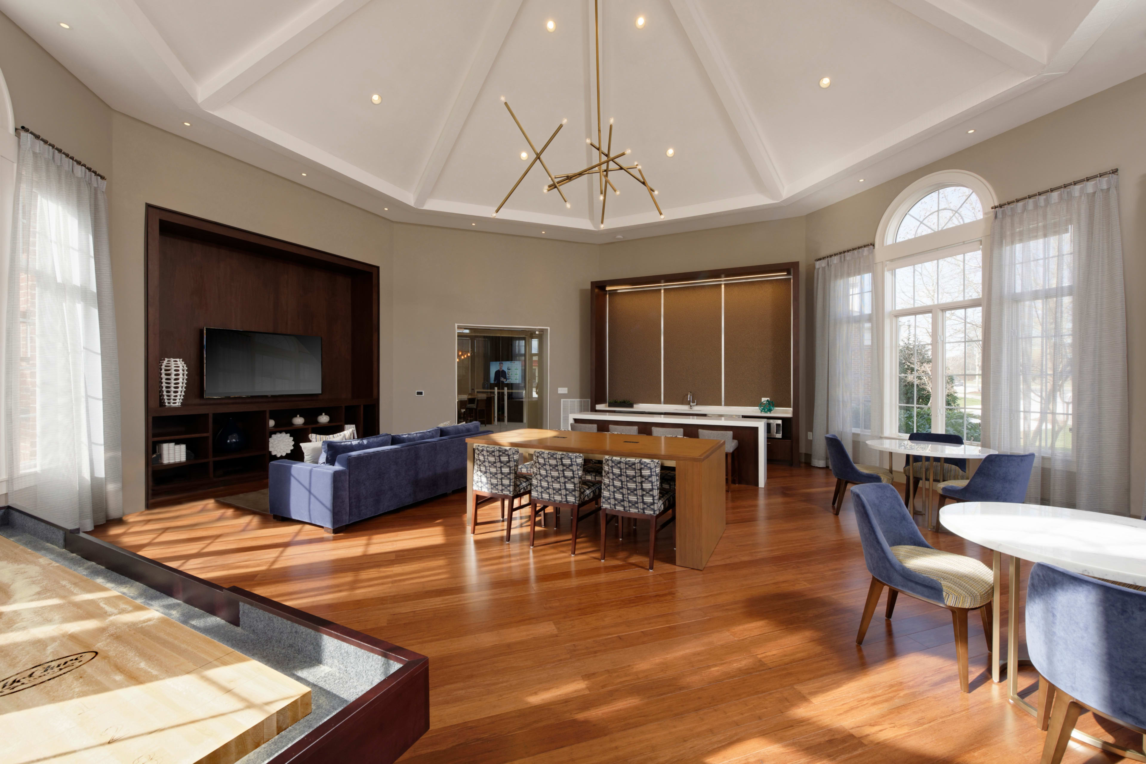 A spacious and modern living area with a high ceiling, featuring a seating area, dining table, and large windows.
