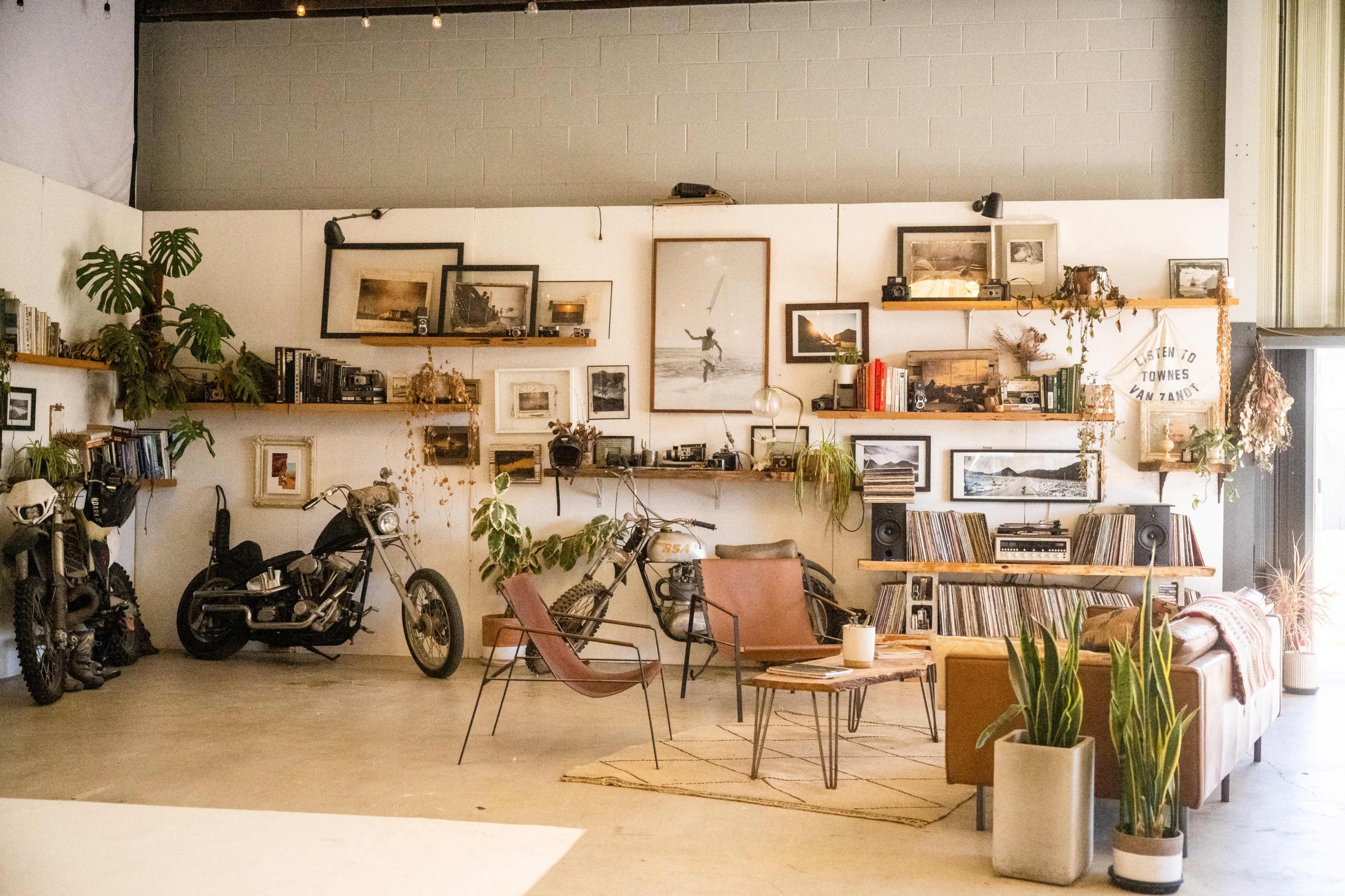 A spacious interior decorated with vintage photographs, plants, and motorcycle-themed decor, featuring a sofa, armchairs, and a record player.