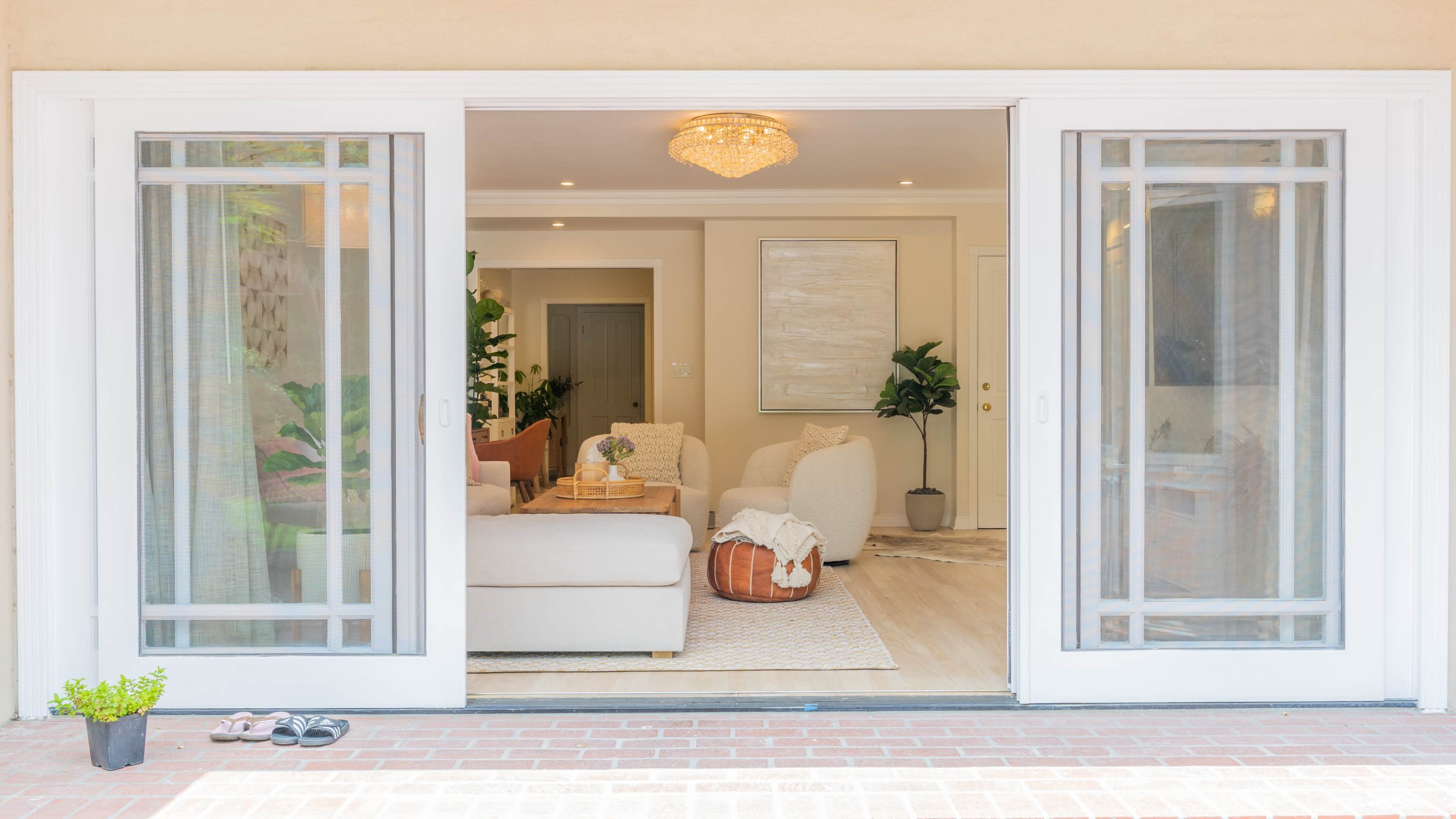 A set of open double doors reveals a bright living room furnished with a light-colored sofa, a decorative basket, and indoor plants.