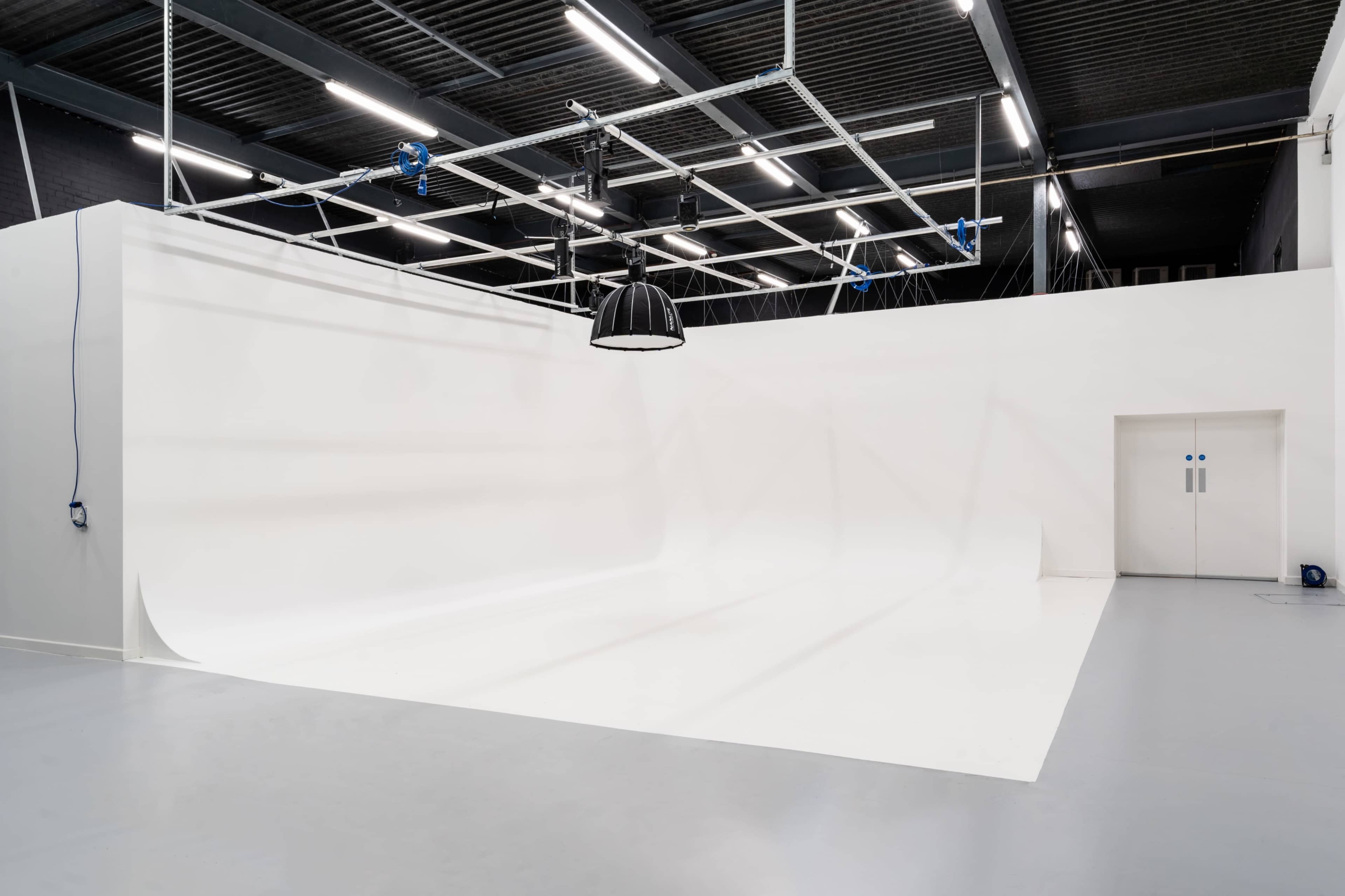 A spacious photography studio with a seamless white backdrop and a door marked with a restroom symbol.