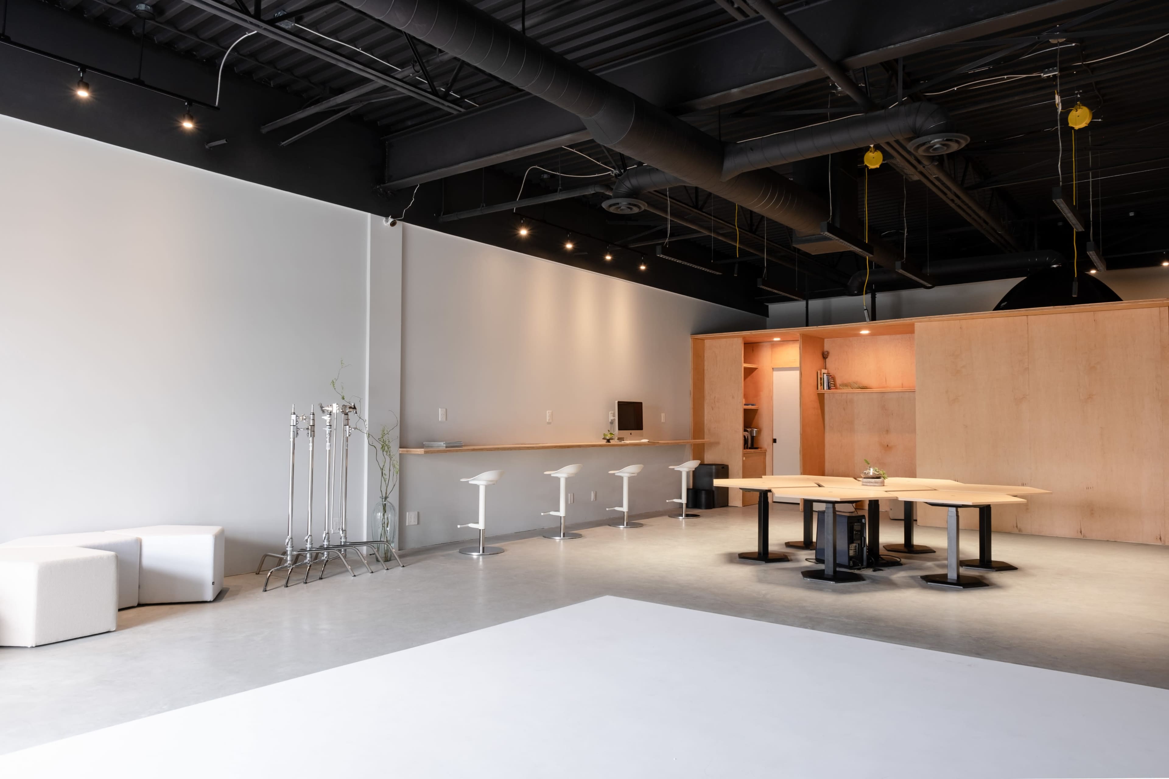 An empty modern office space featuring a large table with chairs, a kitchen area, and minimalistic furniture.