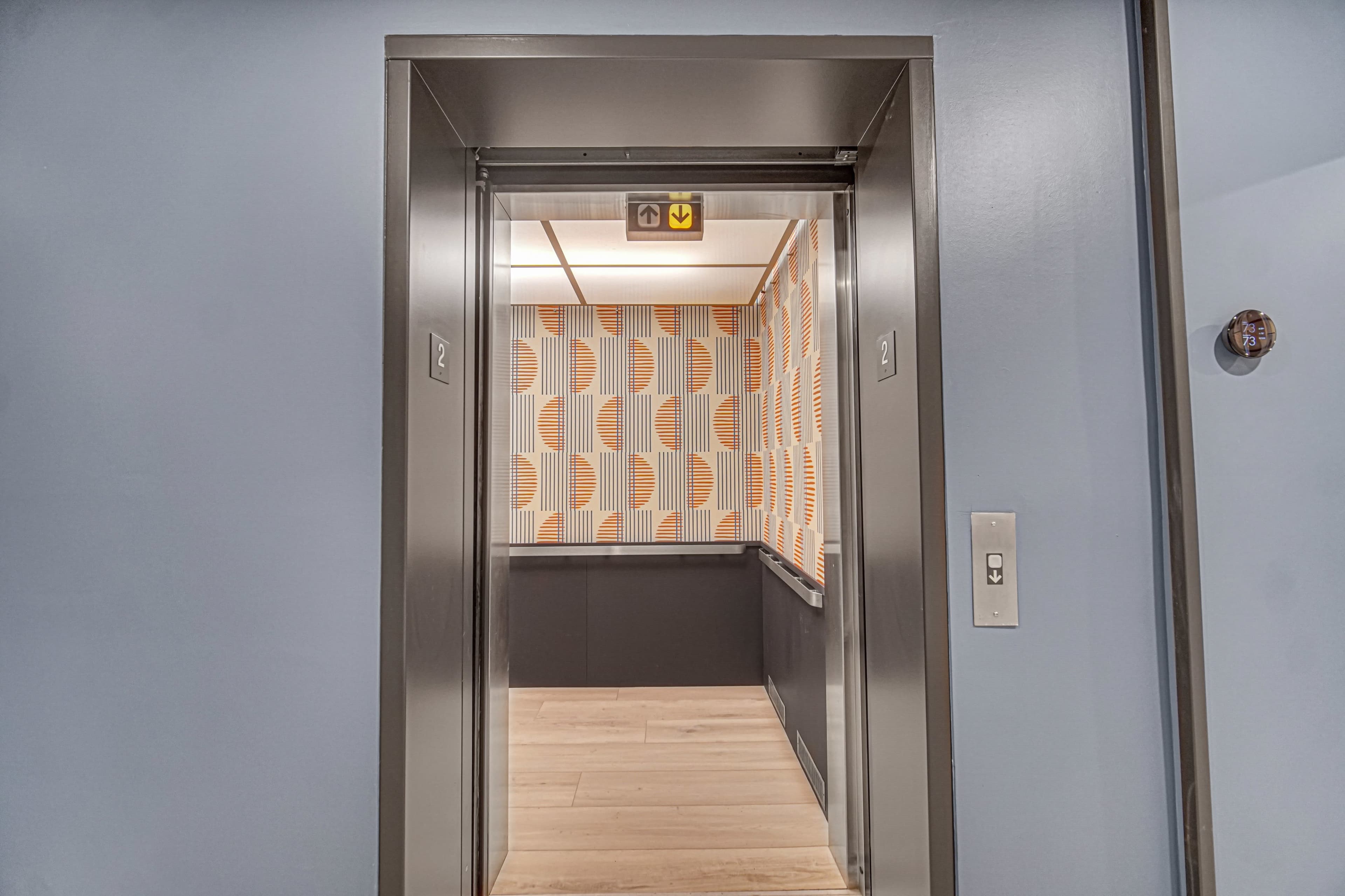 The image shows the open doors of an elevator with a patterned interior and wooden flooring.