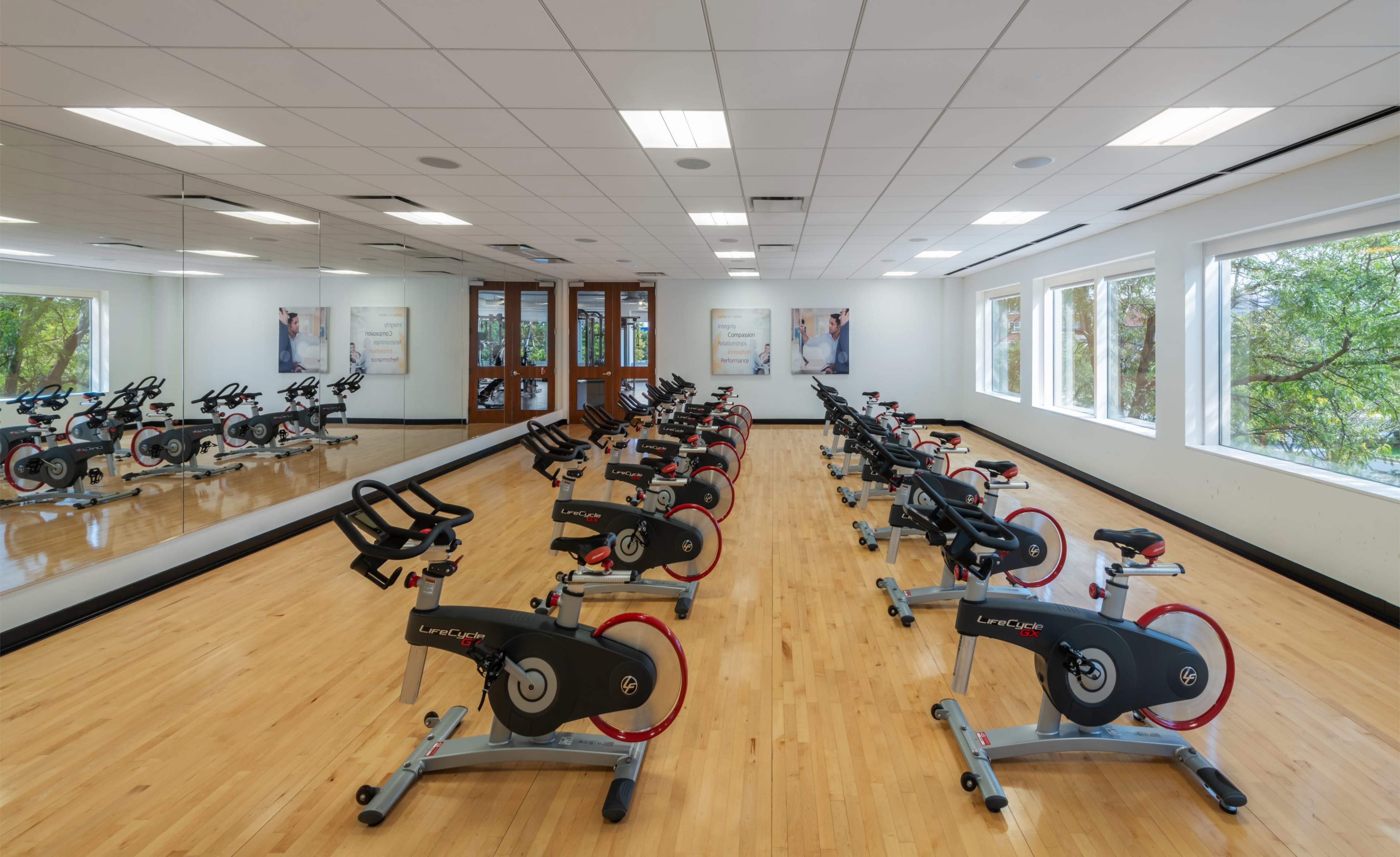 The image shows a fitness studio with rows of stationary bikes facing a mirrored wall and large windows that allow natural light to enter.