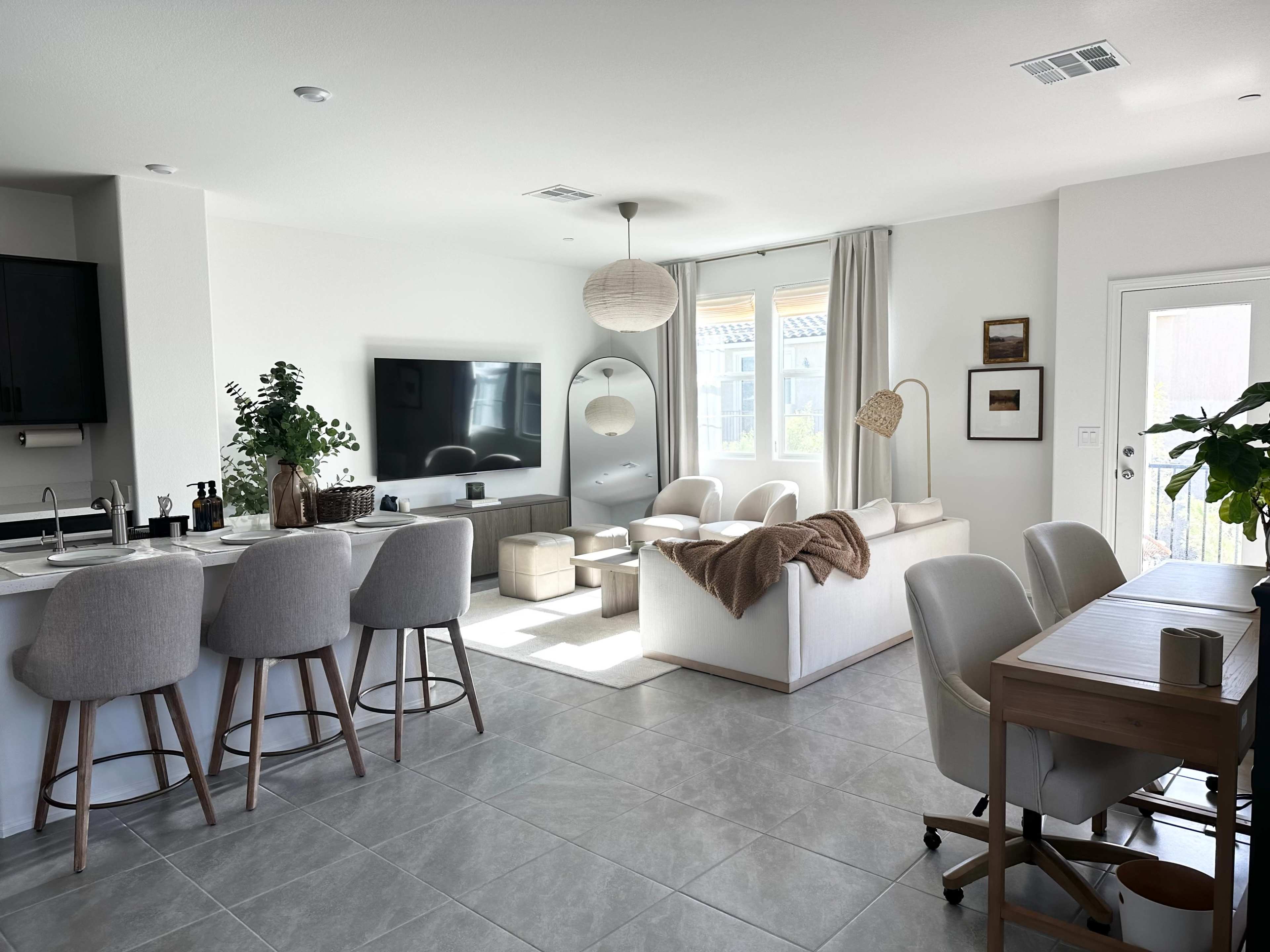 A modern living room and kitchen area with a neutral color scheme, featuring a large TV, a dining table, and comfortable seating.