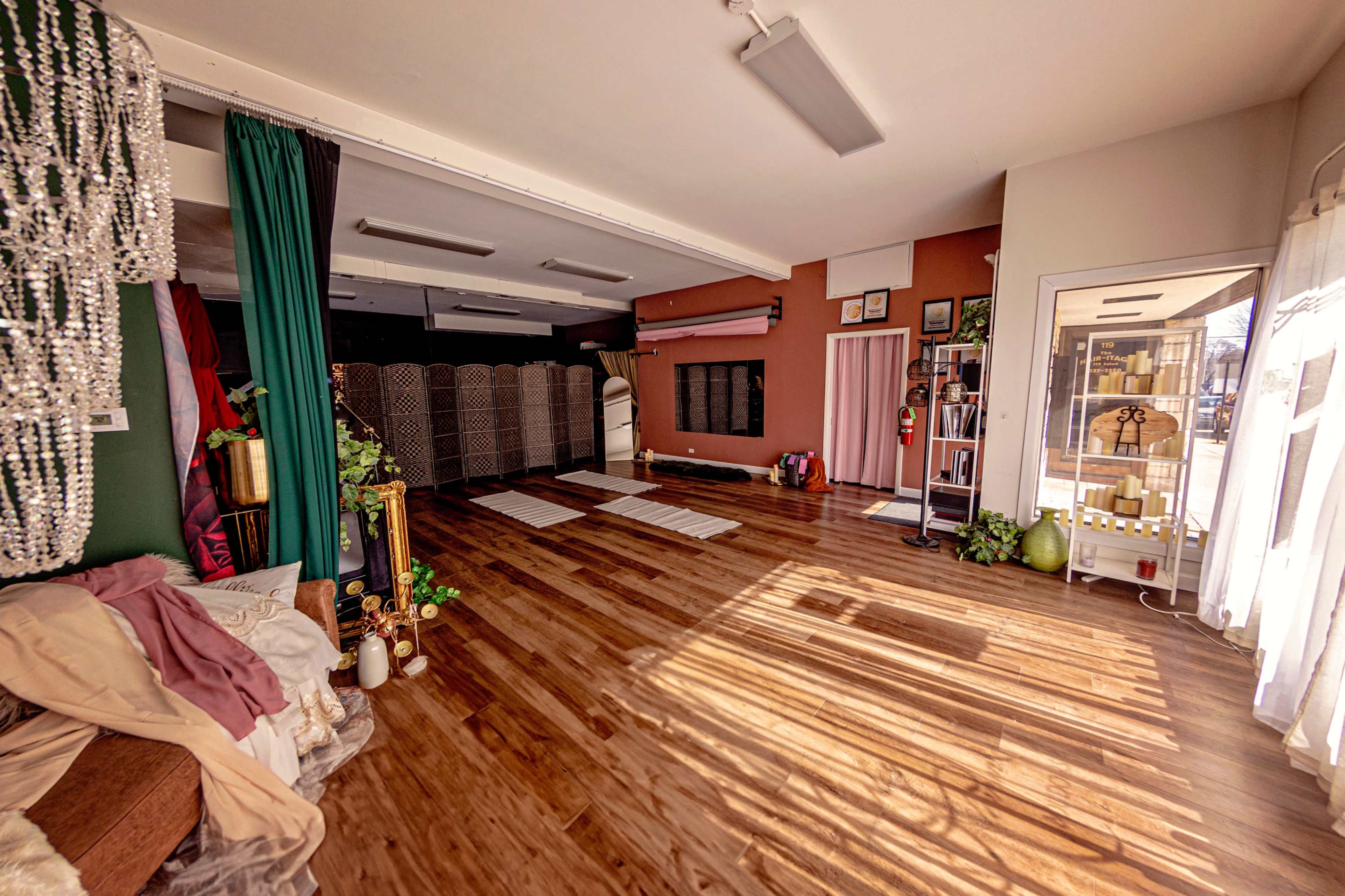 The image shows a spacious interior room with wooden flooring, several decorative partitions, and natural light streaming through large windows.