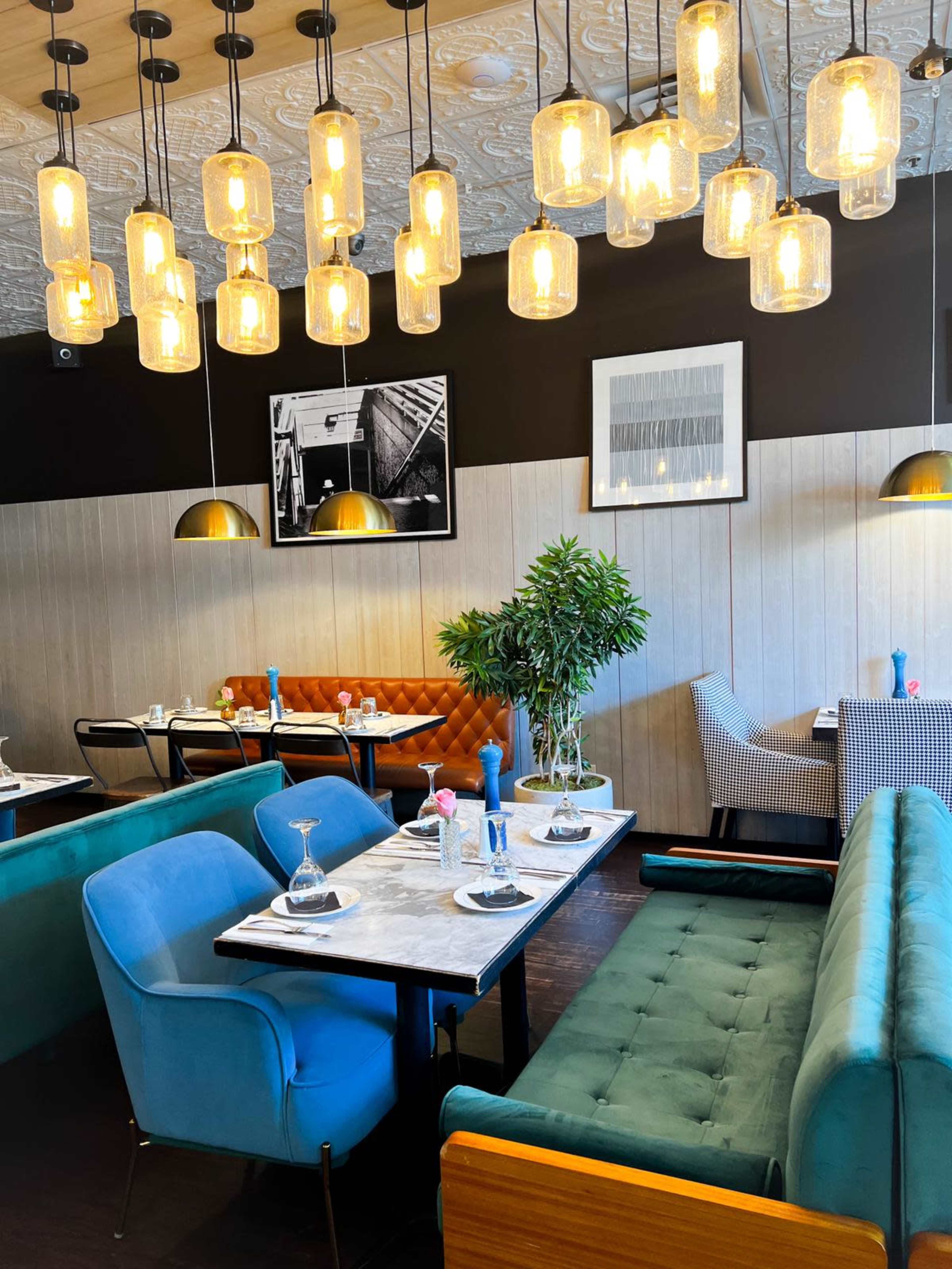 The image shows a modern restaurant interior with teal and orange seating, marble-topped tables, and pendant lights overhead.