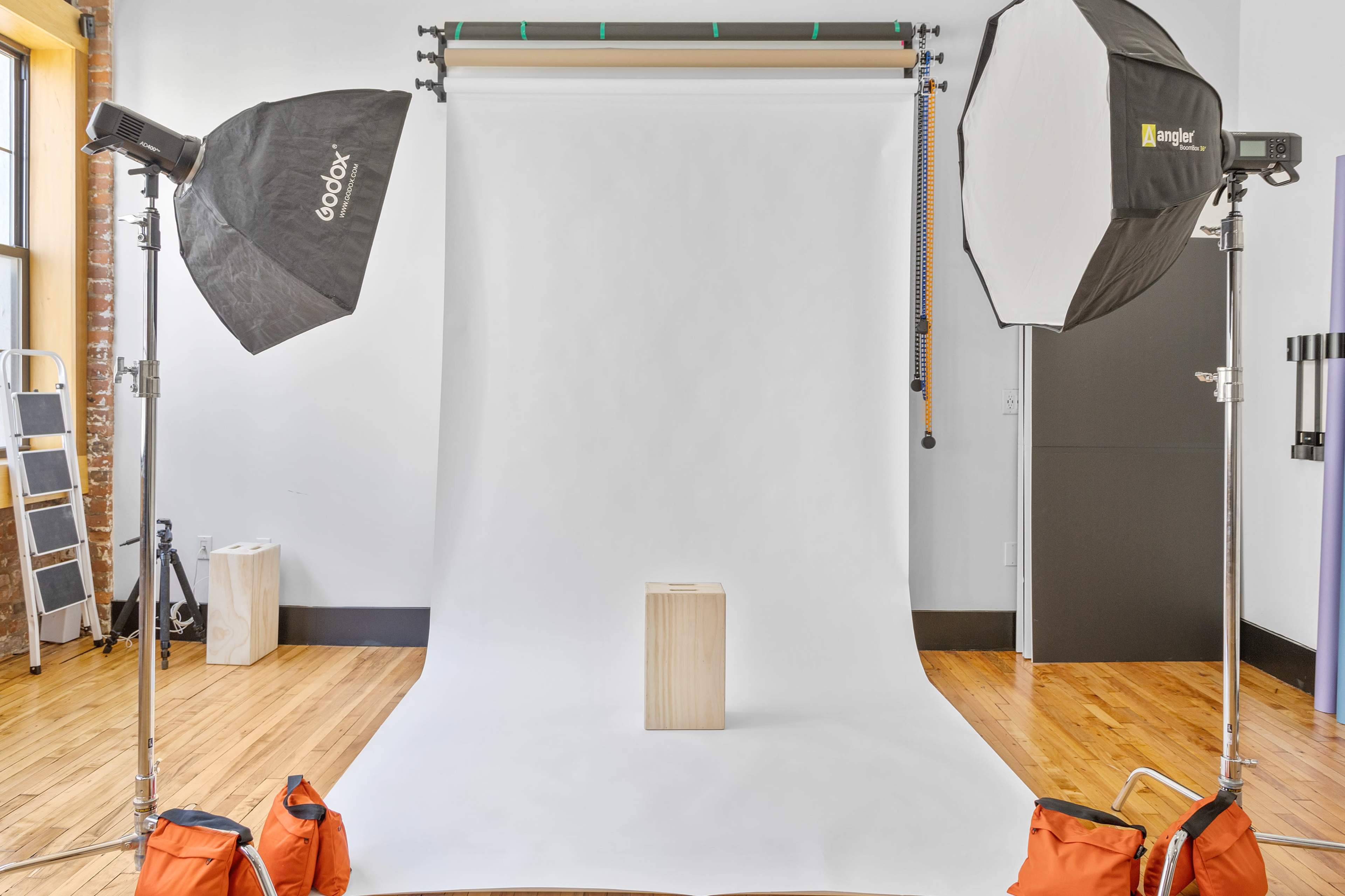 A photography studio is set up with two softbox lights and a wooden pedestal on a white backdrop.
