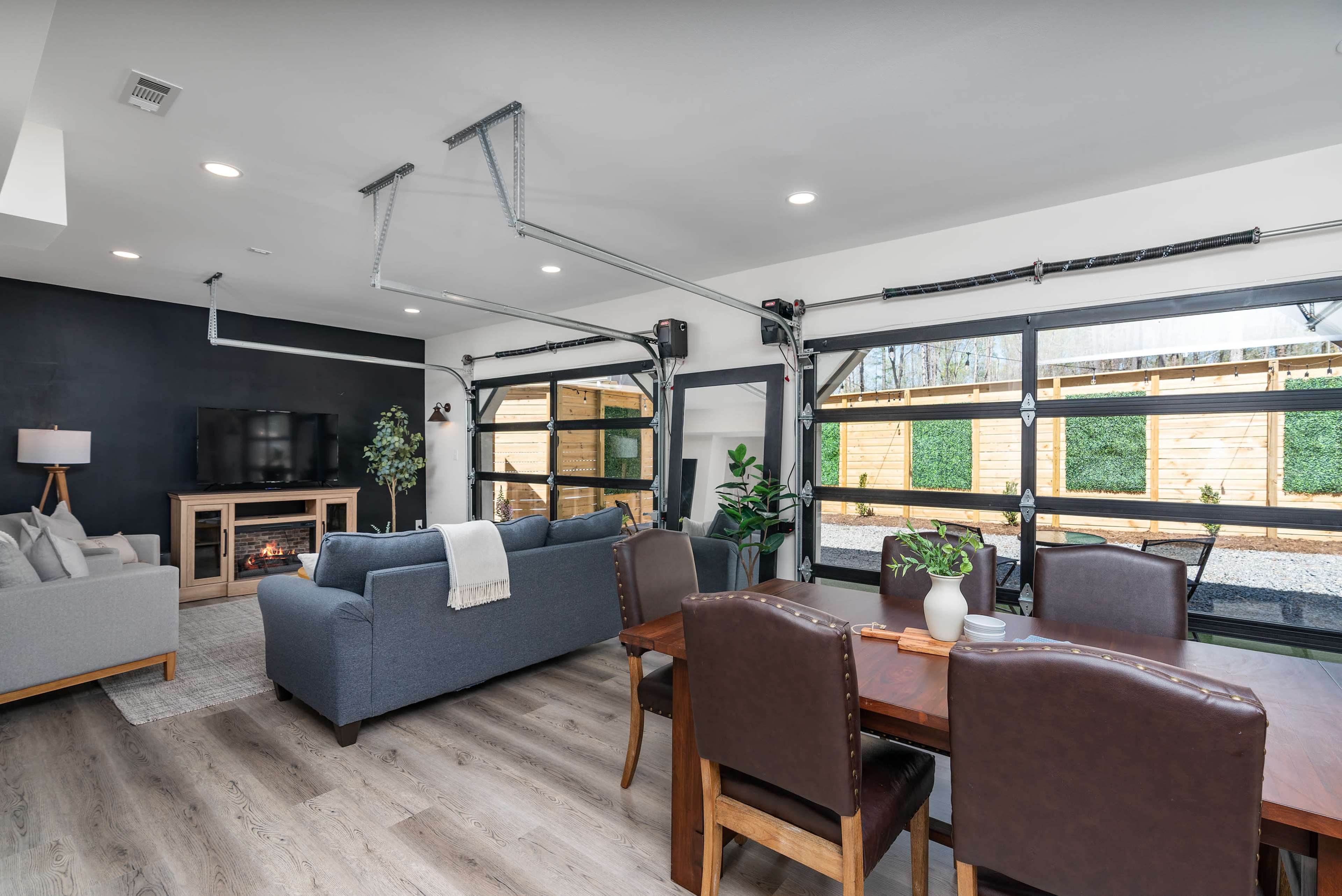 A modern living space with a seating area, dining table, and large garage-style doors leading to an outdoor space.