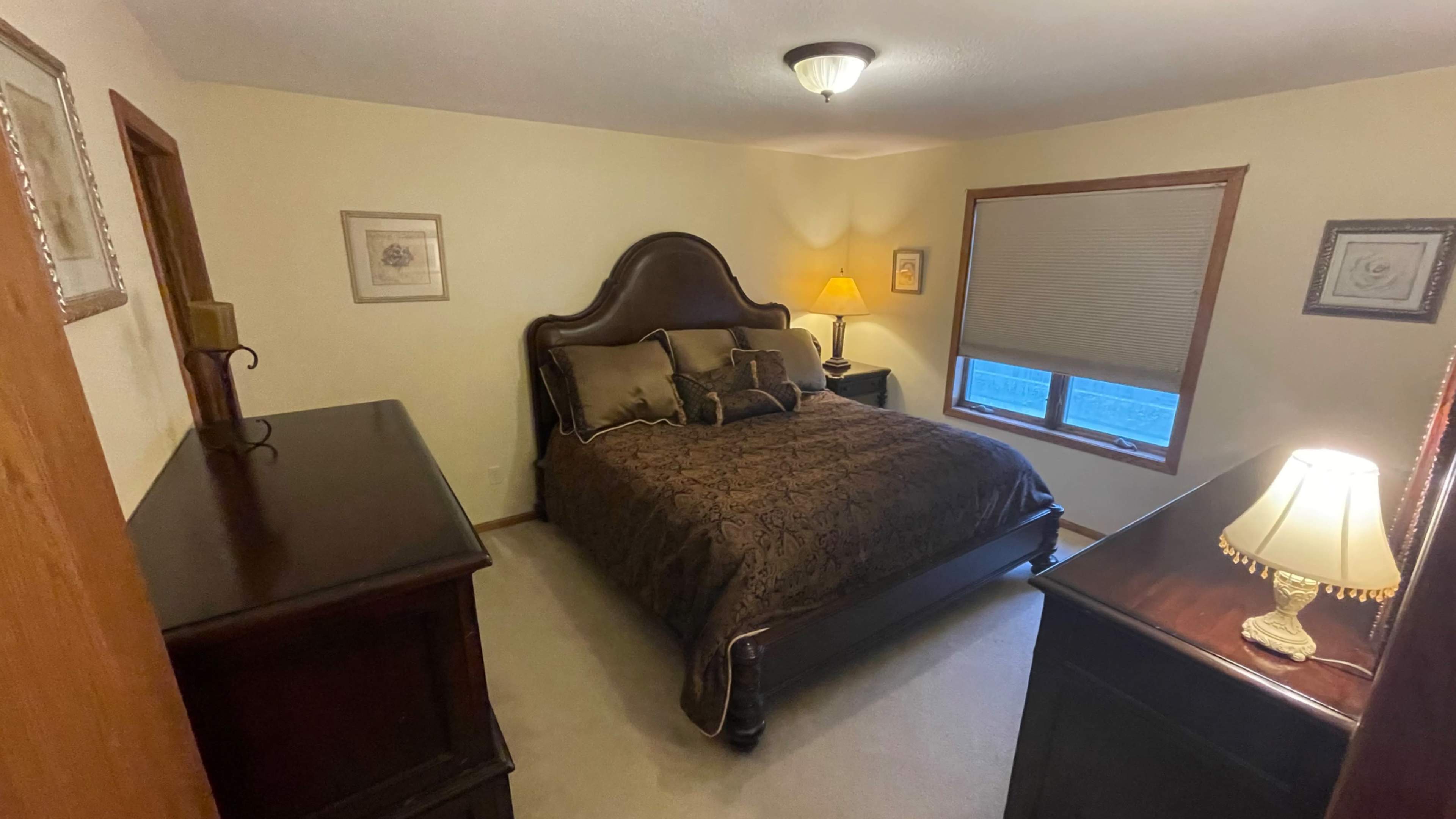A cozy bedroom featuring a dark wooden bed with a patterned brown bedspread, a nightstand with a lamp, and a dresser against the wall.