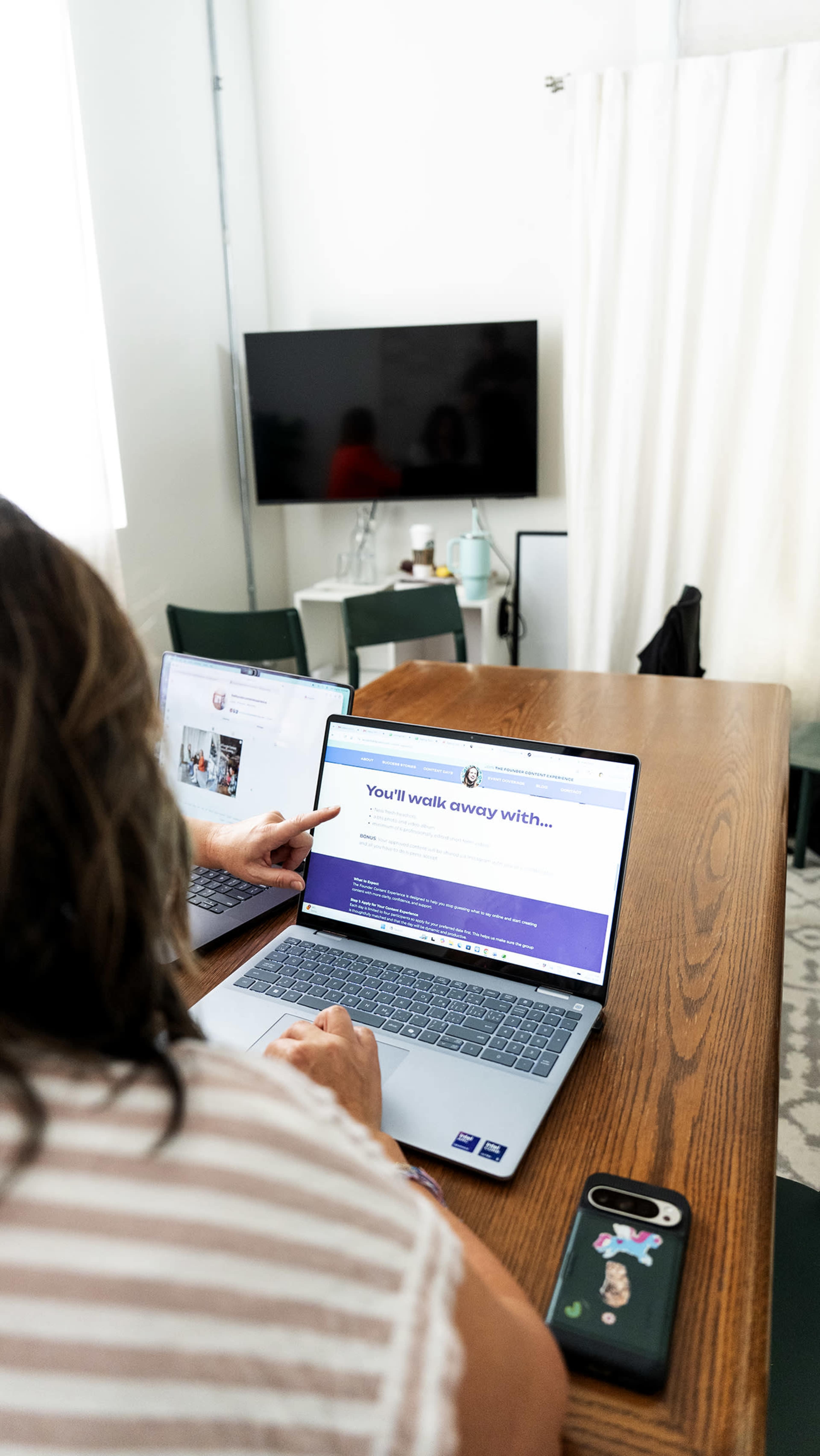 A person is using a laptop on a wooden table while pointing at a webpage displayed on the screen.