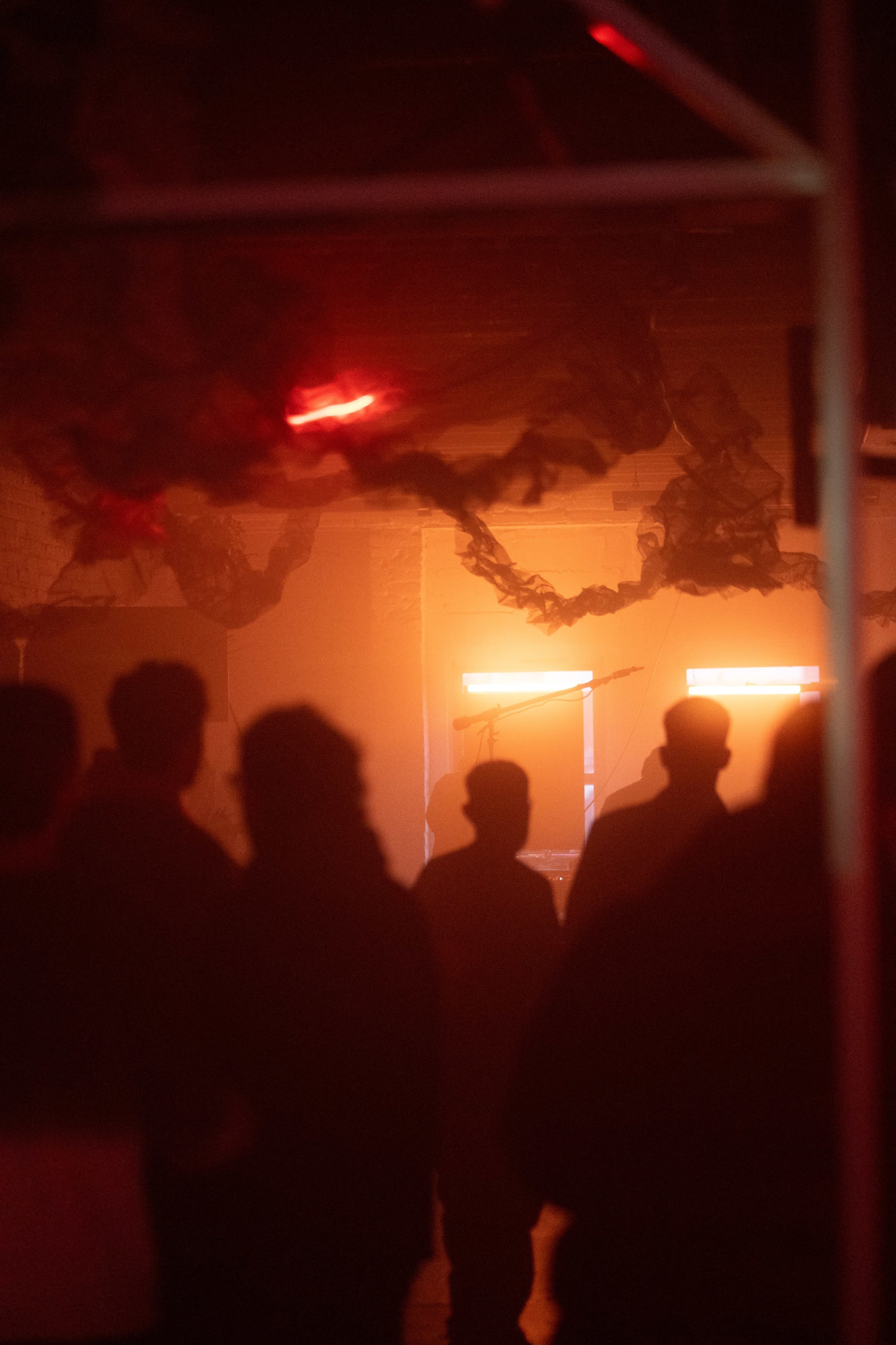 A crowd of people stands in low light, with soft red lighting and dark fabric draping the ceiling.
