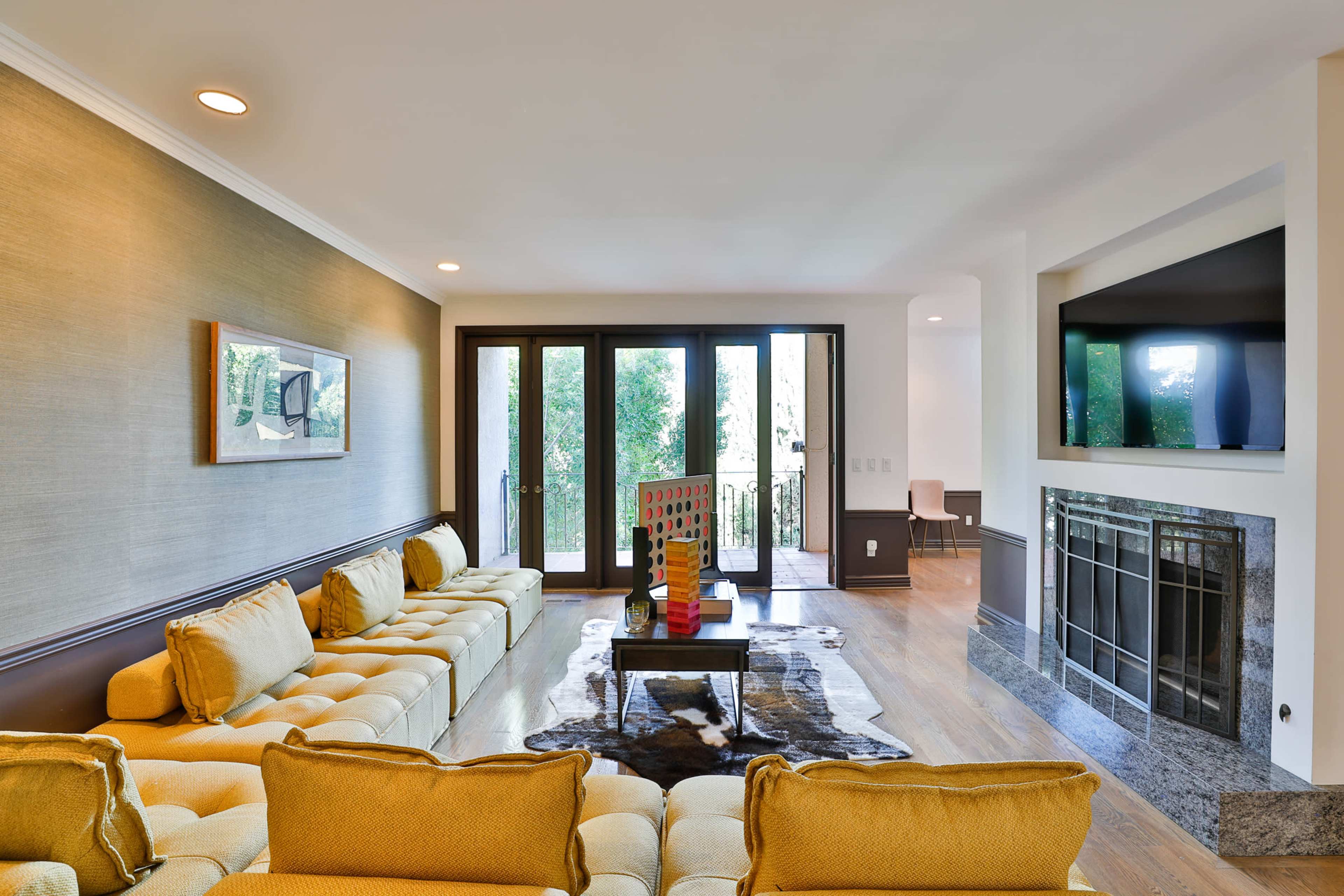 The image shows a living room featuring a yellow tufted sofa, a modern coffee table, a stone fireplace, and large glass doors opening to a balcony.