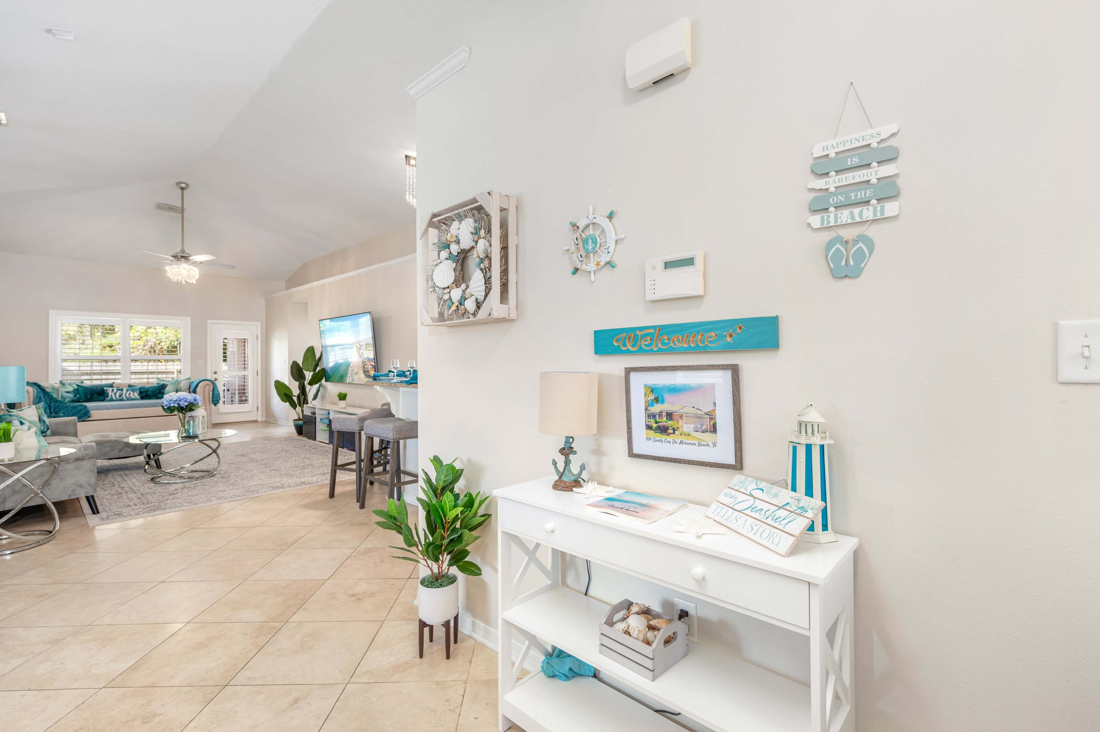 A bright interior entryway with a console table, decorative wall art, and a view into a living area featuring light-colored furnishings.