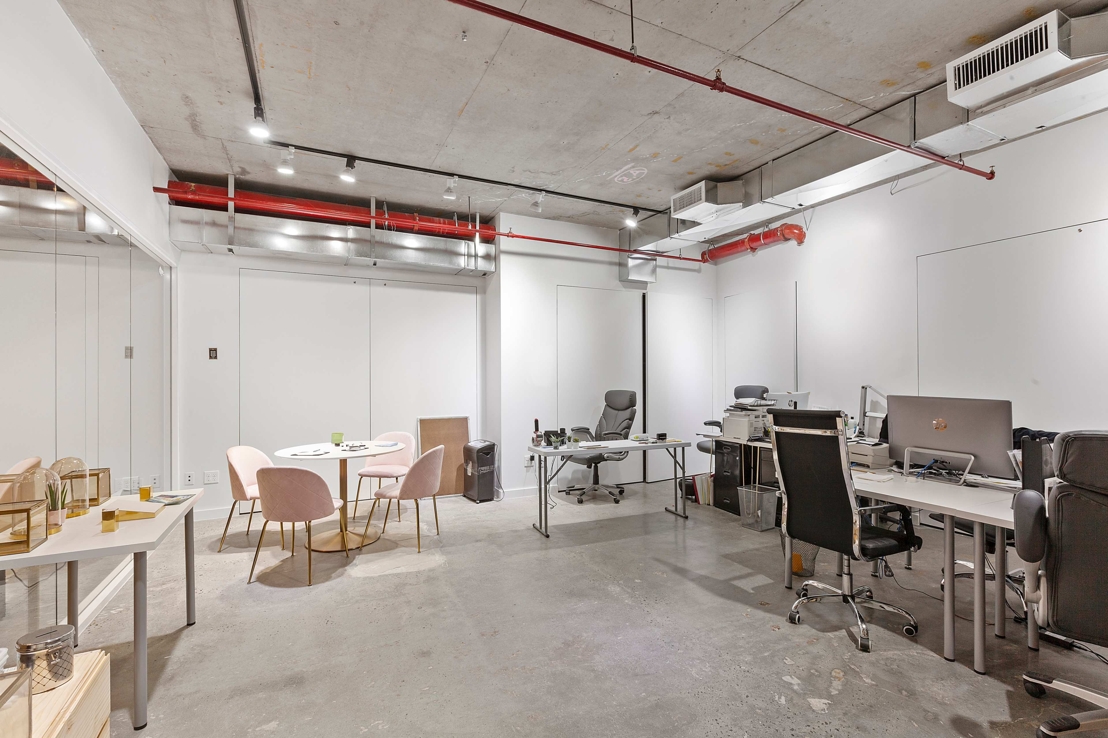 The image shows a modern office space with workstations, a meeting table with chairs, and exposed concrete ceilings.