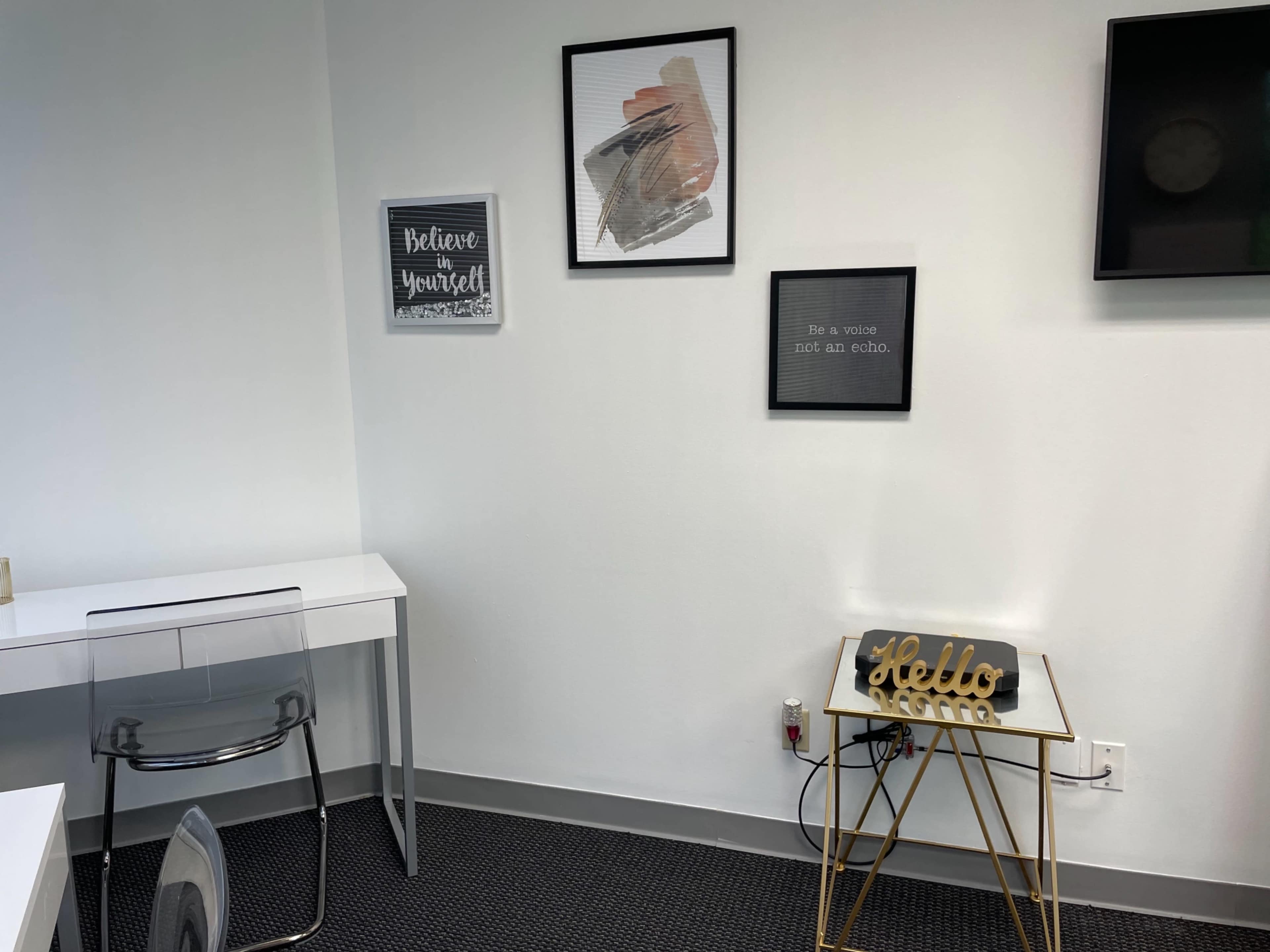 A minimalist office space with a clear desk, two framed motivational posters on the wall, and a small table displaying a decorative "Hello" sign.