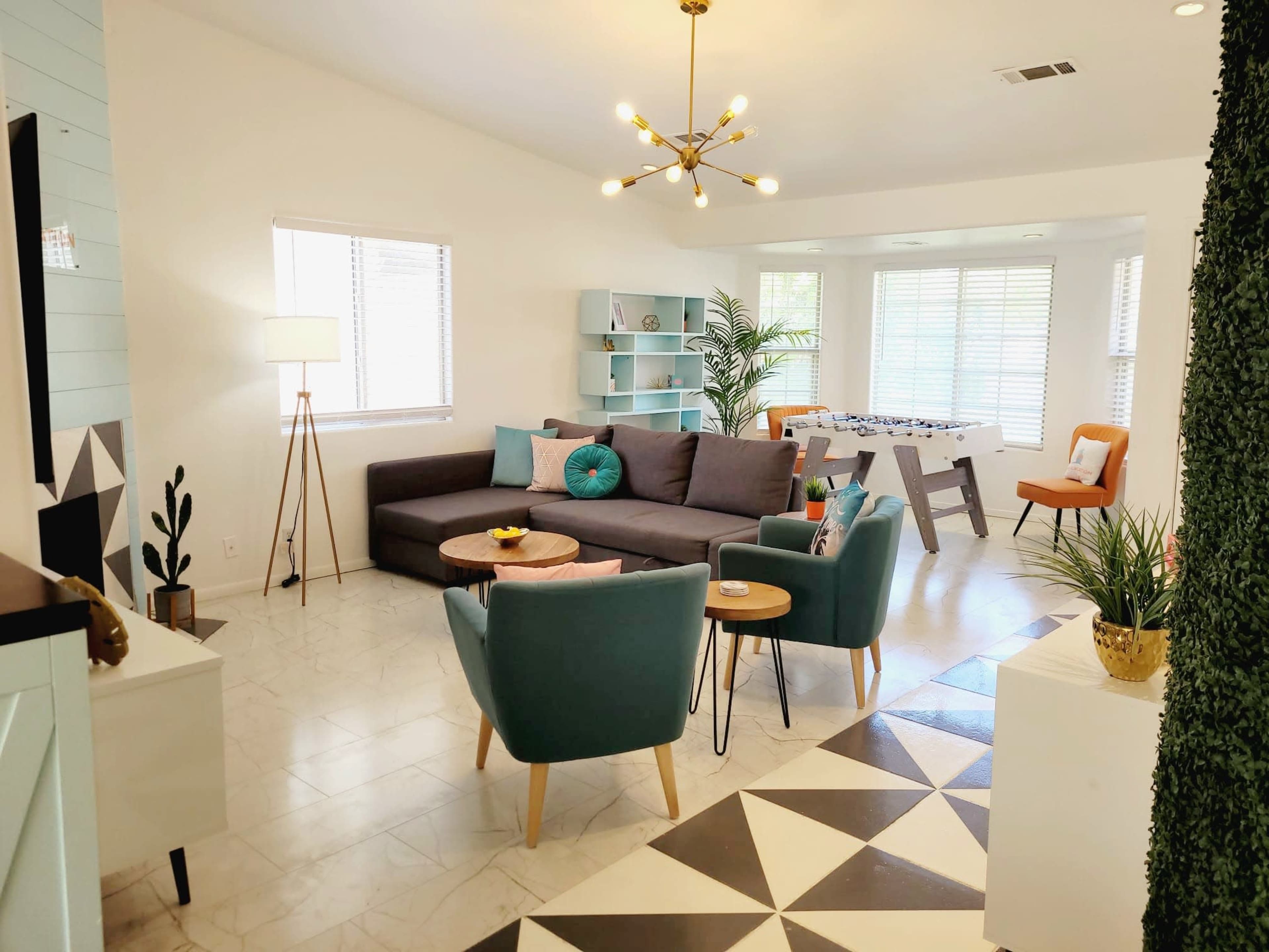 A modern living room with a gray sectional sofa, a round coffee table, and a bright, open space featuring a game table and decorative shelving.