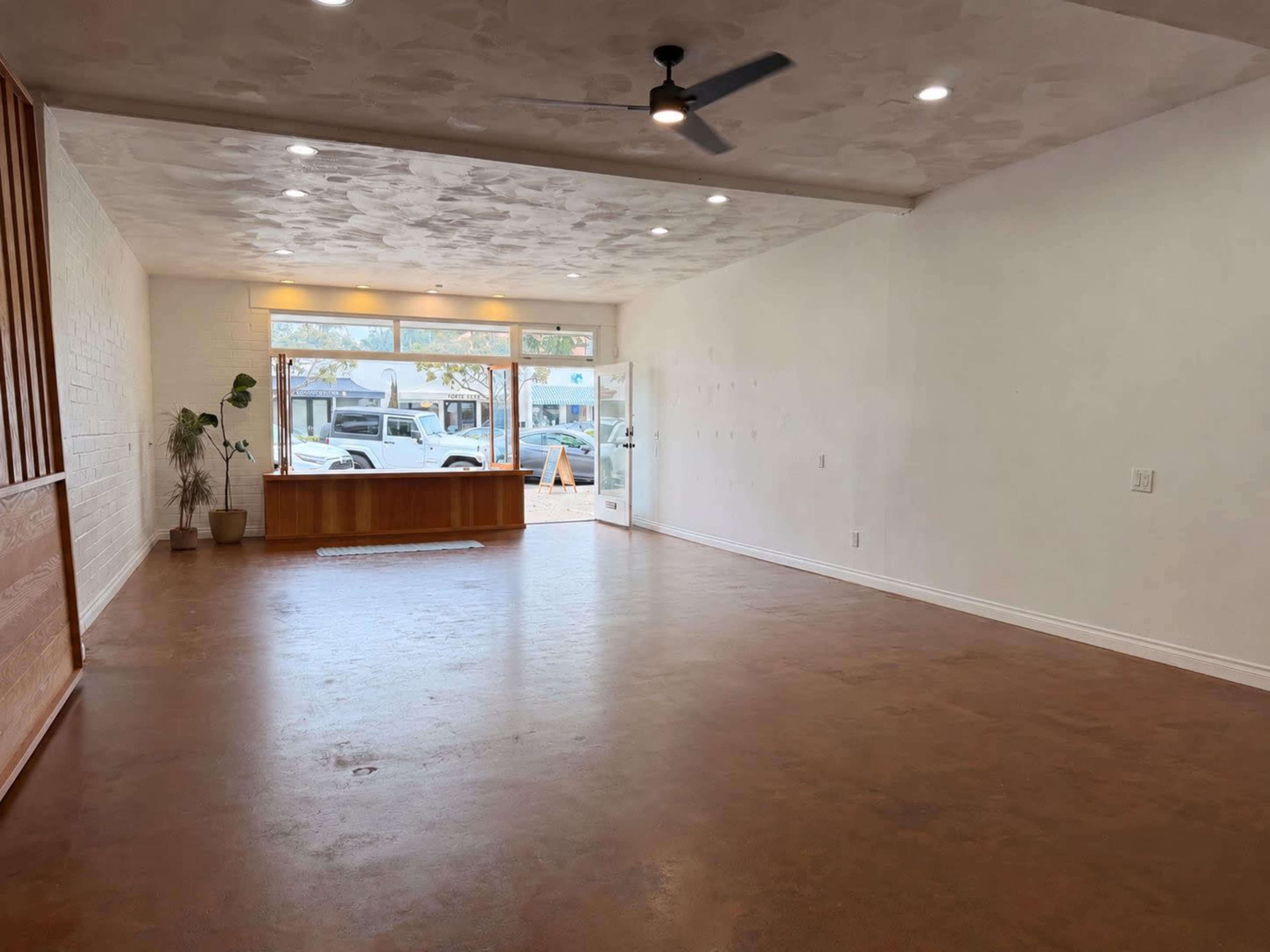 The image shows an empty interior space with a smooth, light-colored floor and a large window facing the street, allowing natural light to enter.