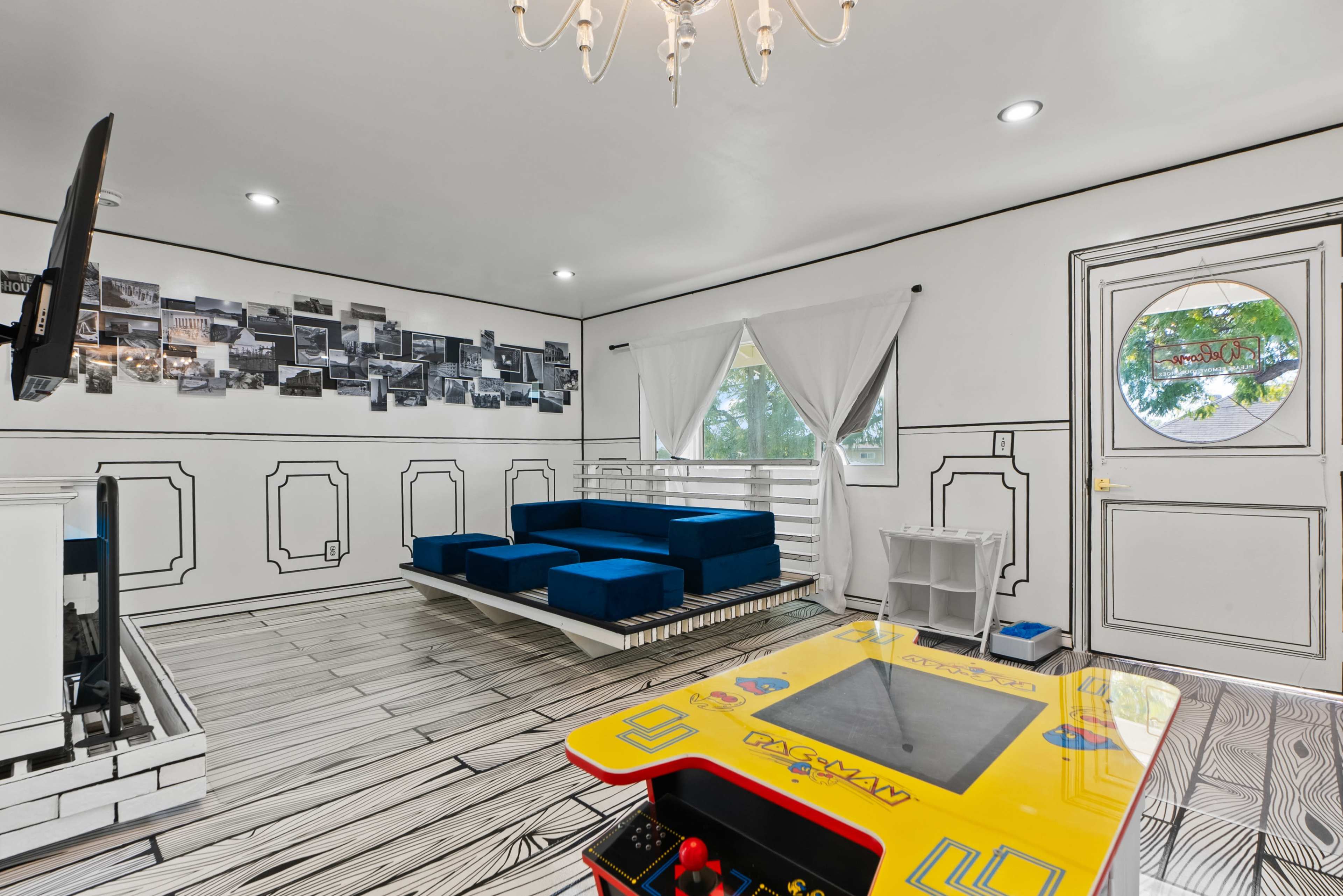 The room features a modern design with a blue couch, a vintage arcade game table, and a gallery wall of black and white photographs.