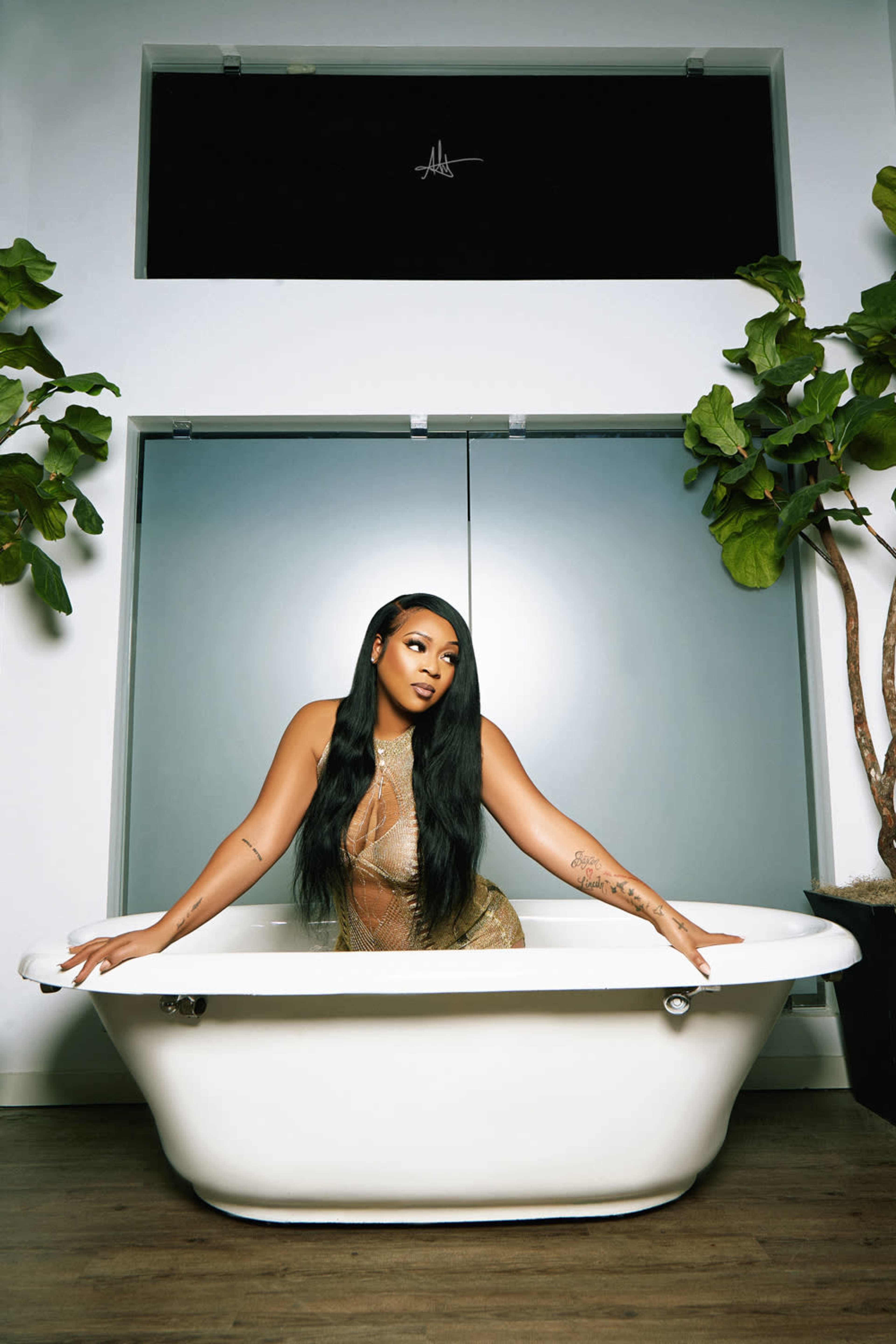 A person poses in a white bathtub surrounded by potted plants in a modern interior.