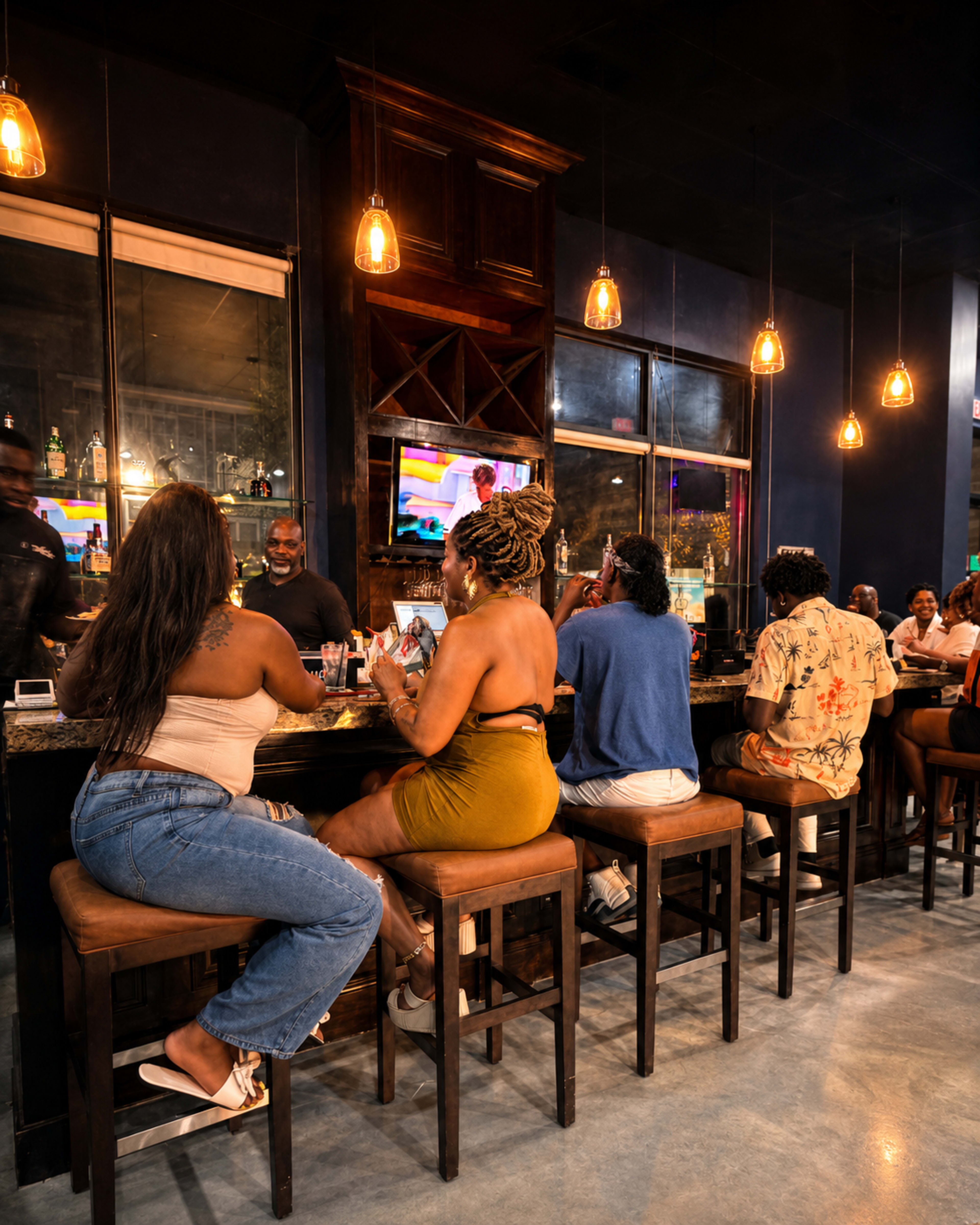 A group of people sits at a bar, enjoying drinks and watching a television screen, with warm lighting and a lively atmosphere.