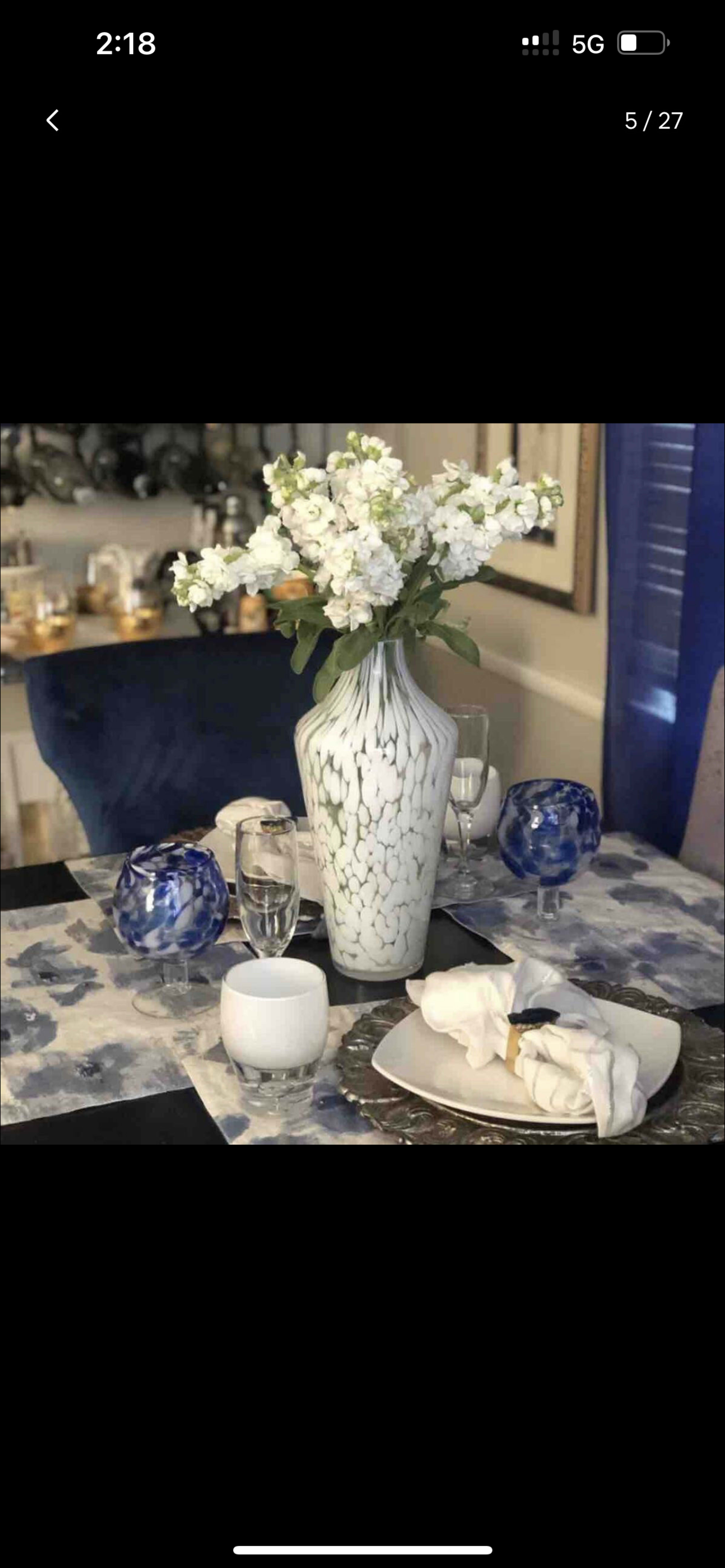 A dining table is set with a patterned tablecloth, a vase of white flowers, and decorative bowls.