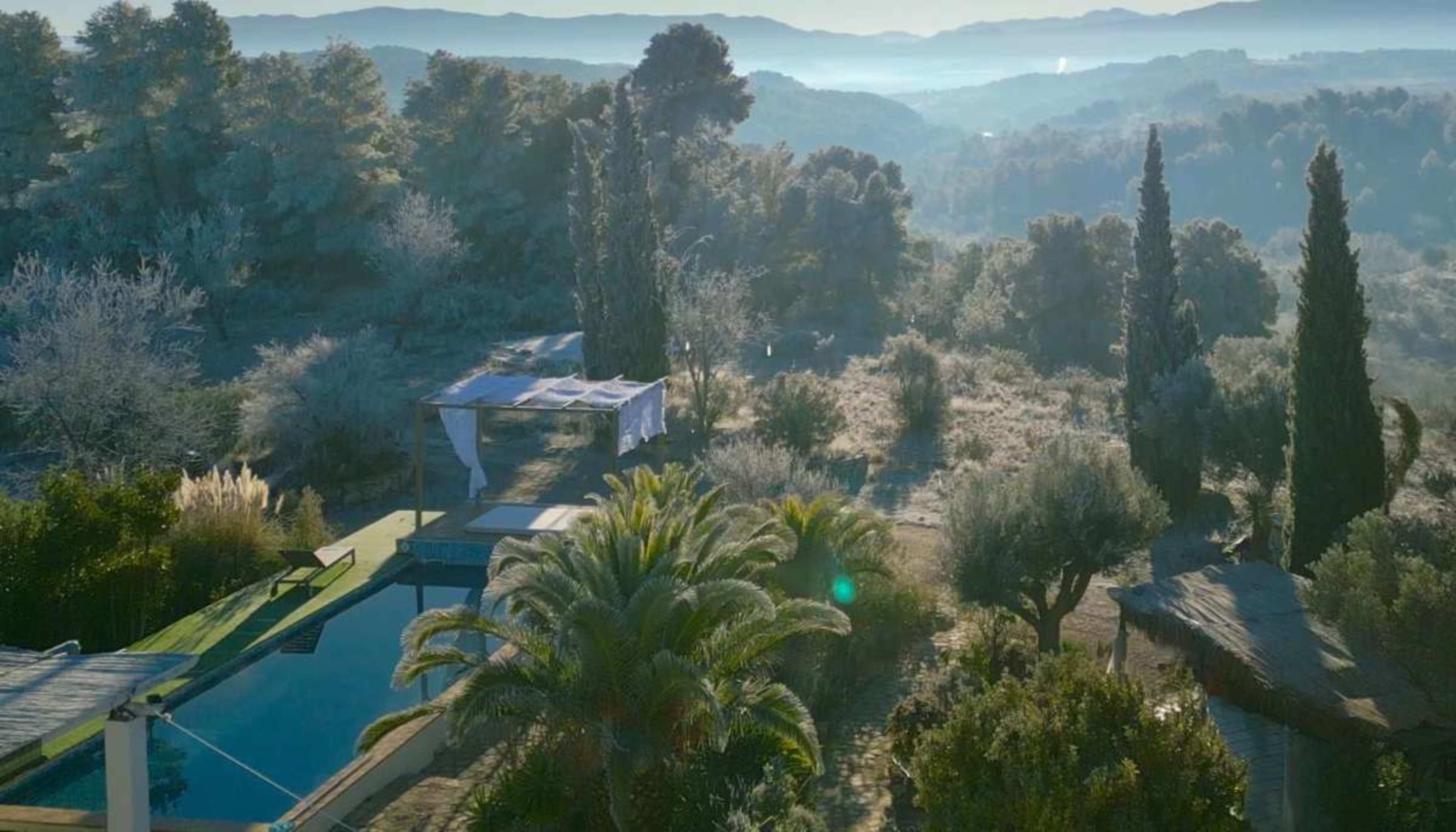 The image shows a lush outdoor area with a swimming pool surrounded by trees and hills in the background.