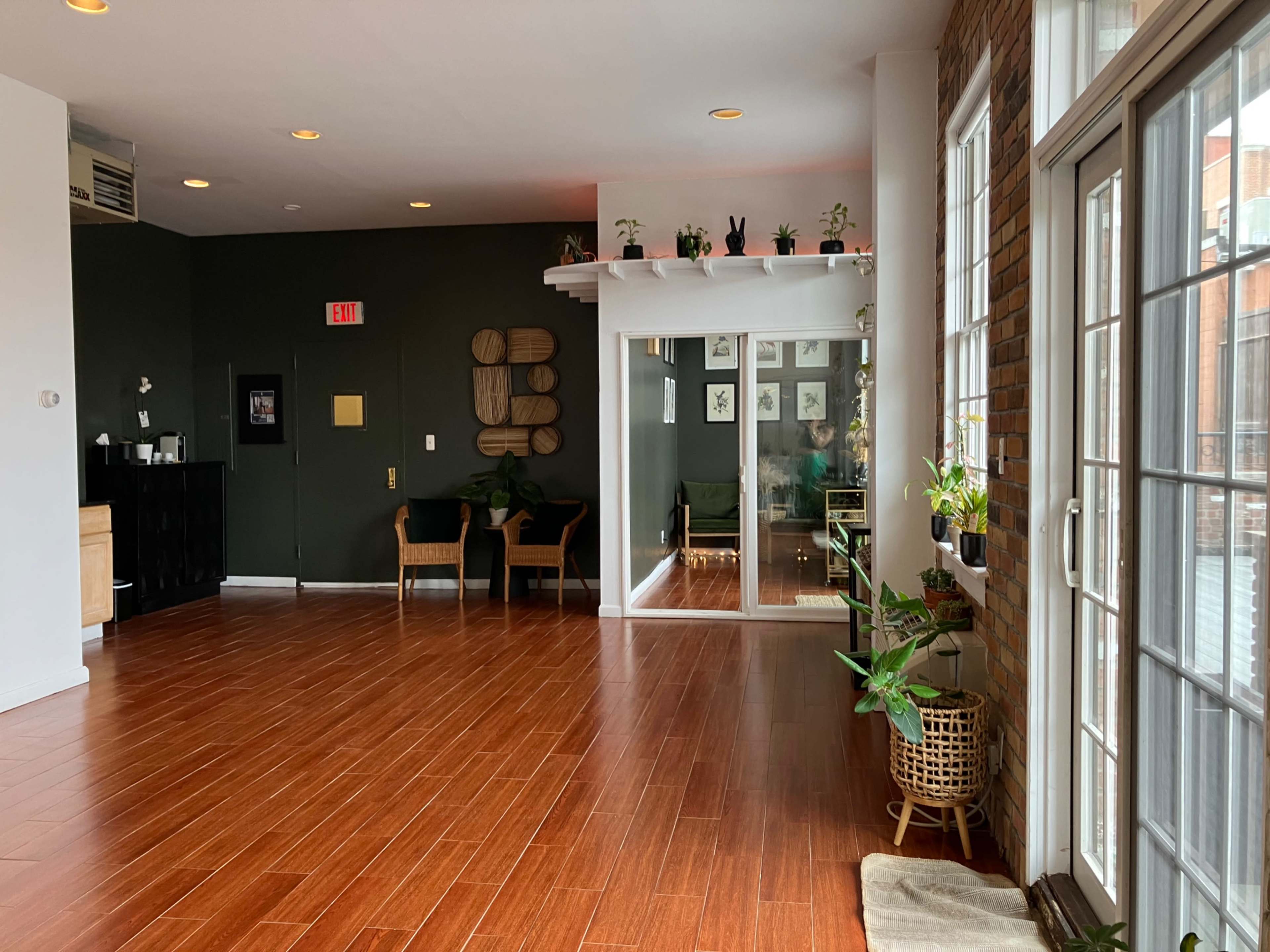 A spacious room features wooden floors, potted plants, and large windows that open to another area.