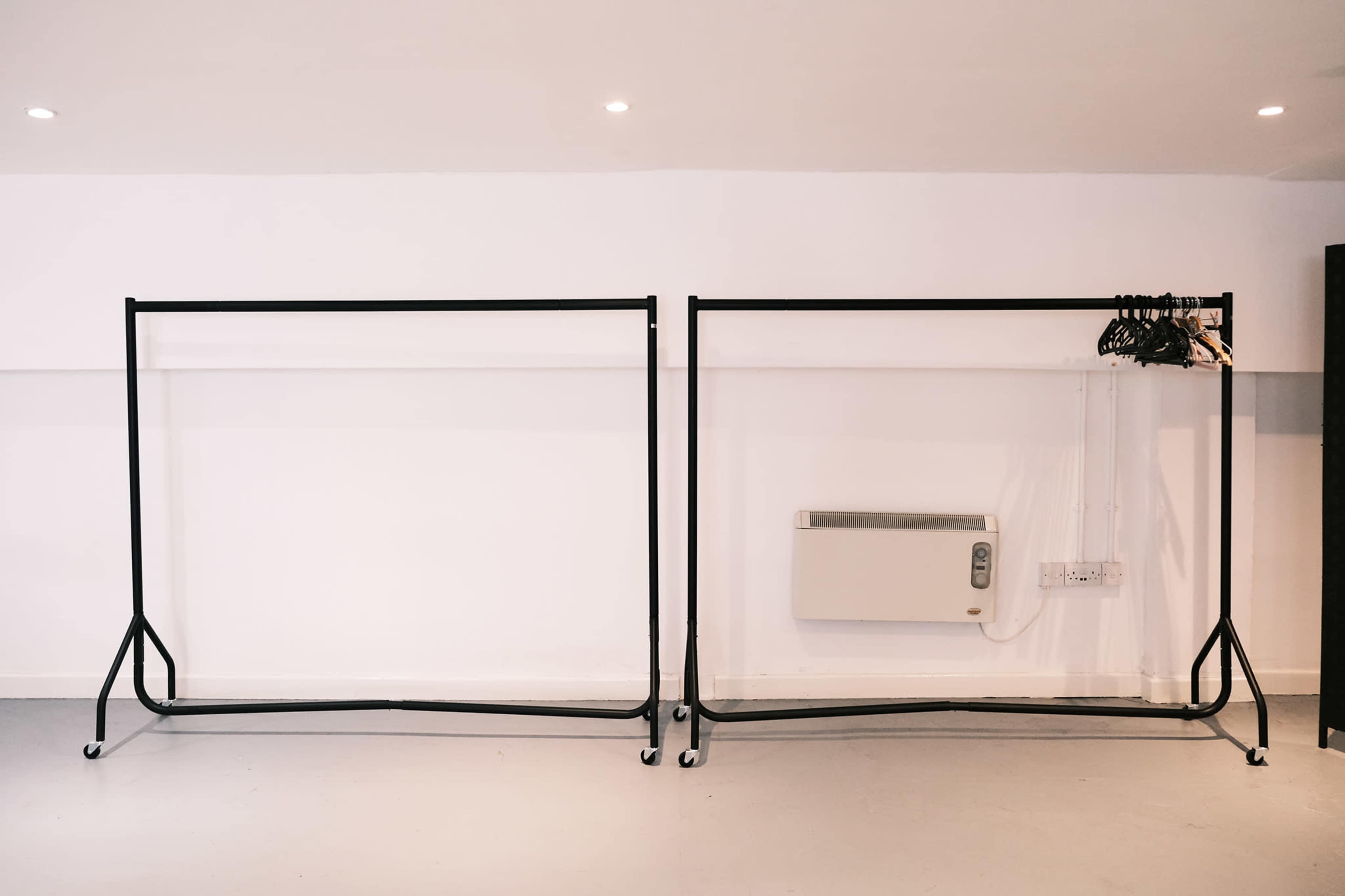 Two clothing racks are positioned against a plain white wall, with one rack displaying several hangers.