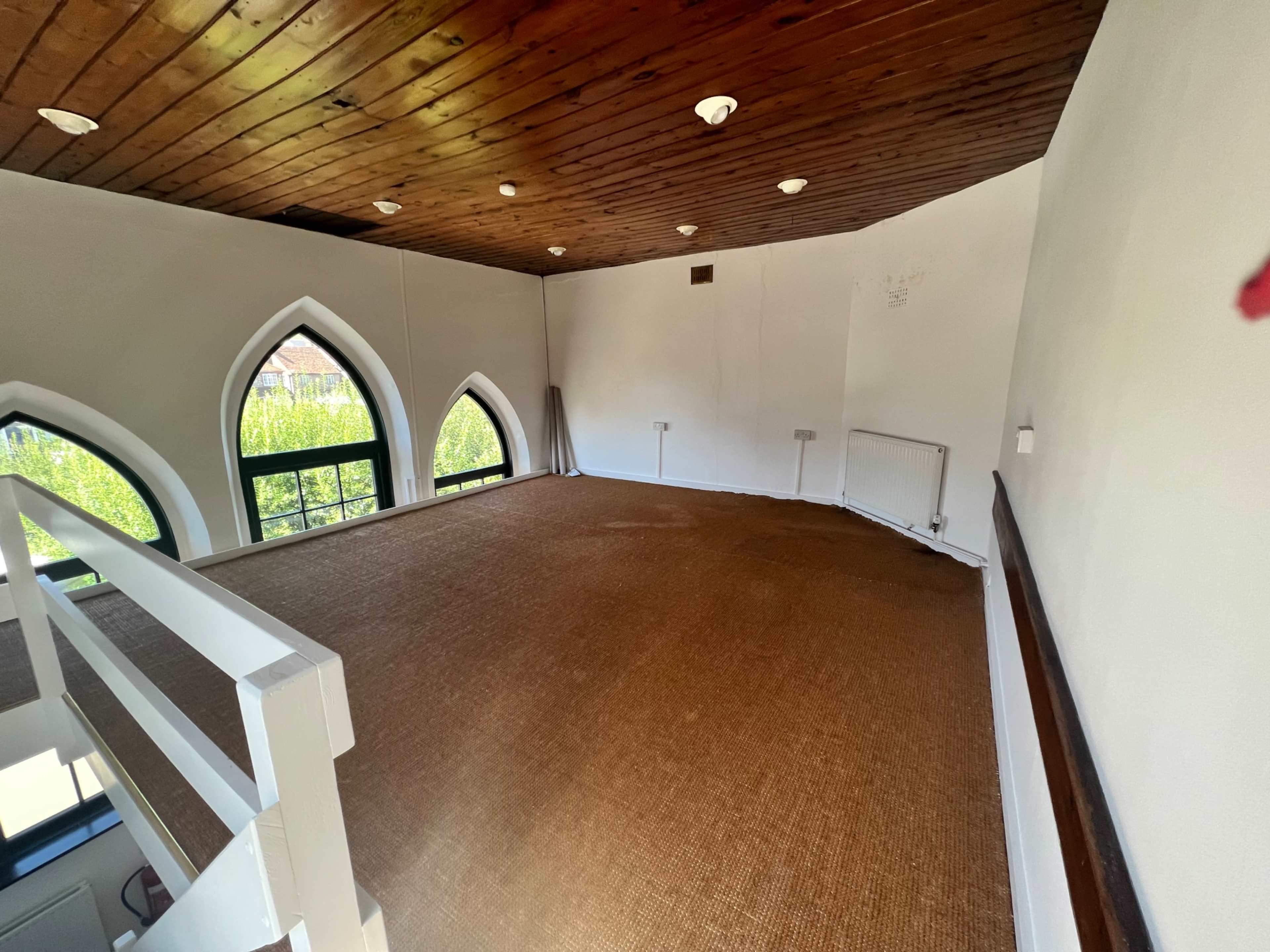 An empty room with a wooden ceiling, large arched windows, and a carpeted floor.