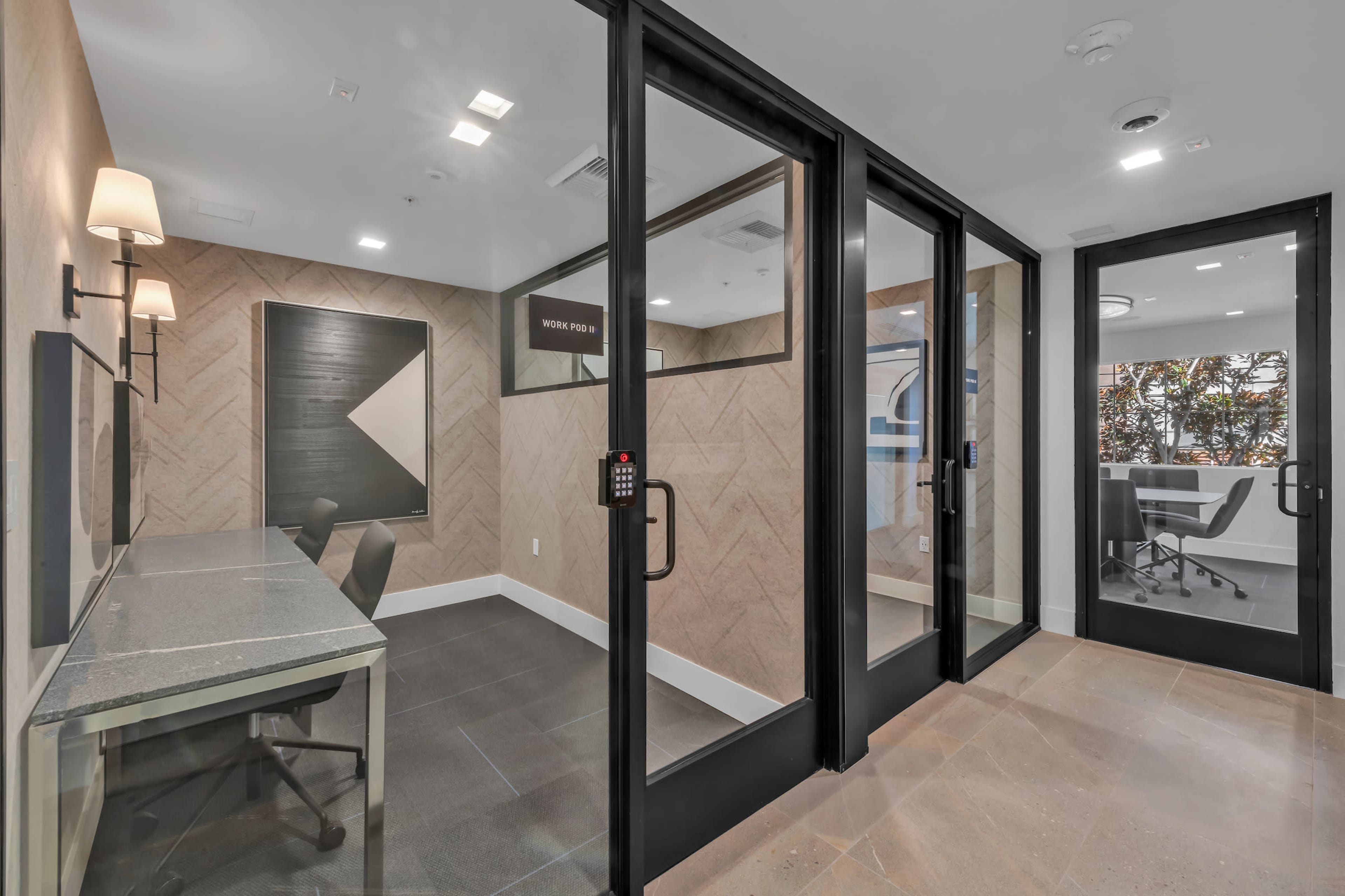 A modern office space with glass walls, featuring a meeting room on one side and a small workspace with two chairs on the other.