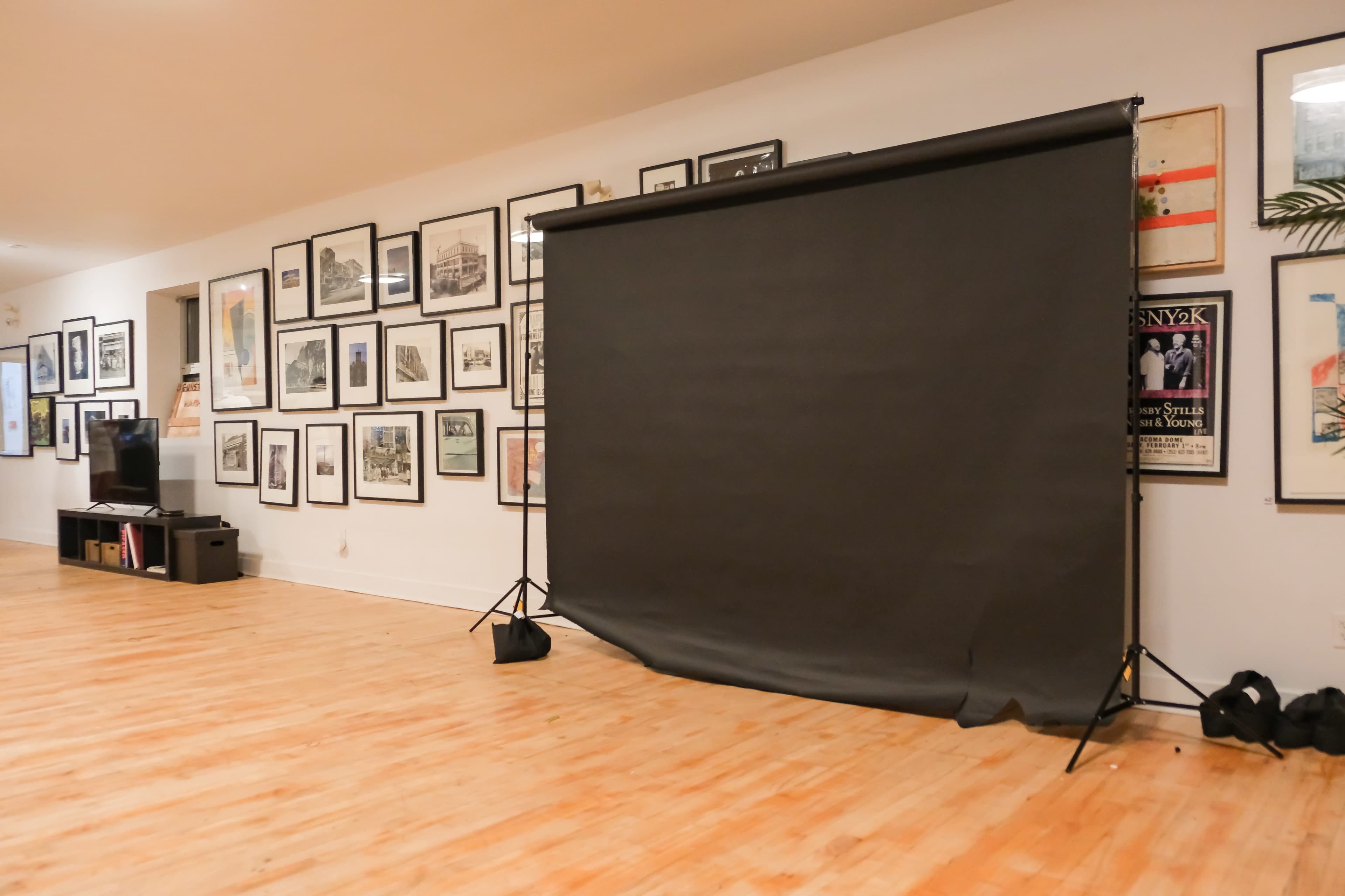 A photography studio features a black backdrop on a stand set against a wall adorned with framed photographs and artworks.